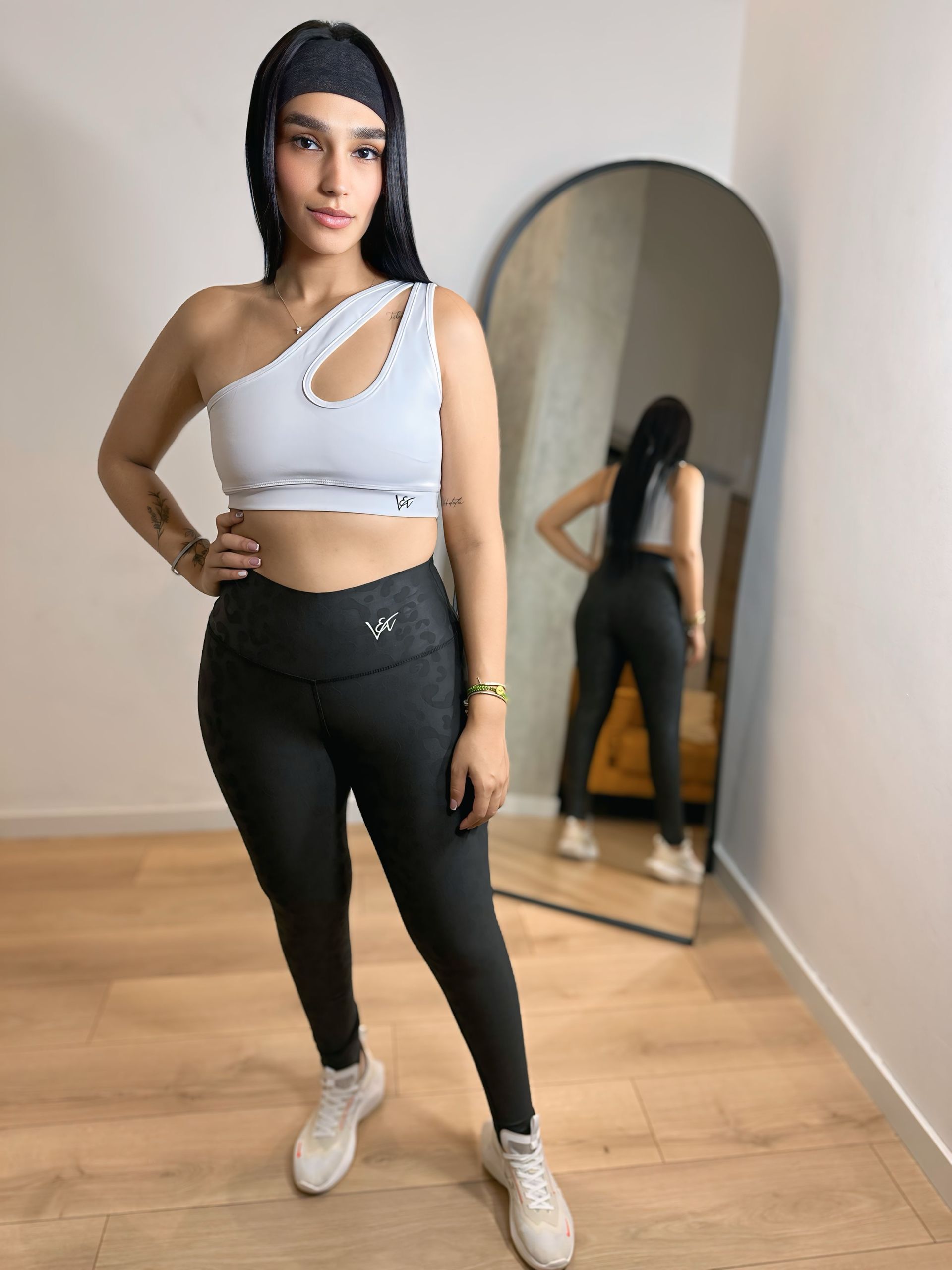 A woman in a white crop top and black leggings is standing in front of a mirror.