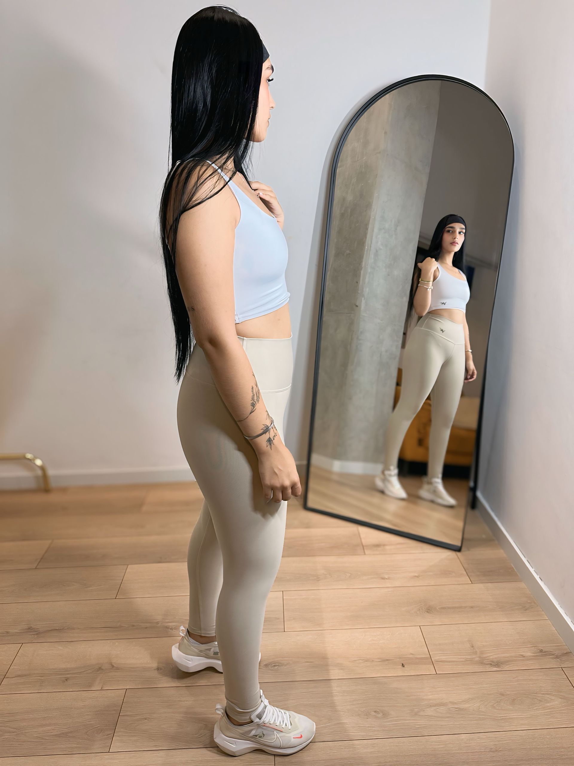 A woman is standing in front of a large mirror in a room.