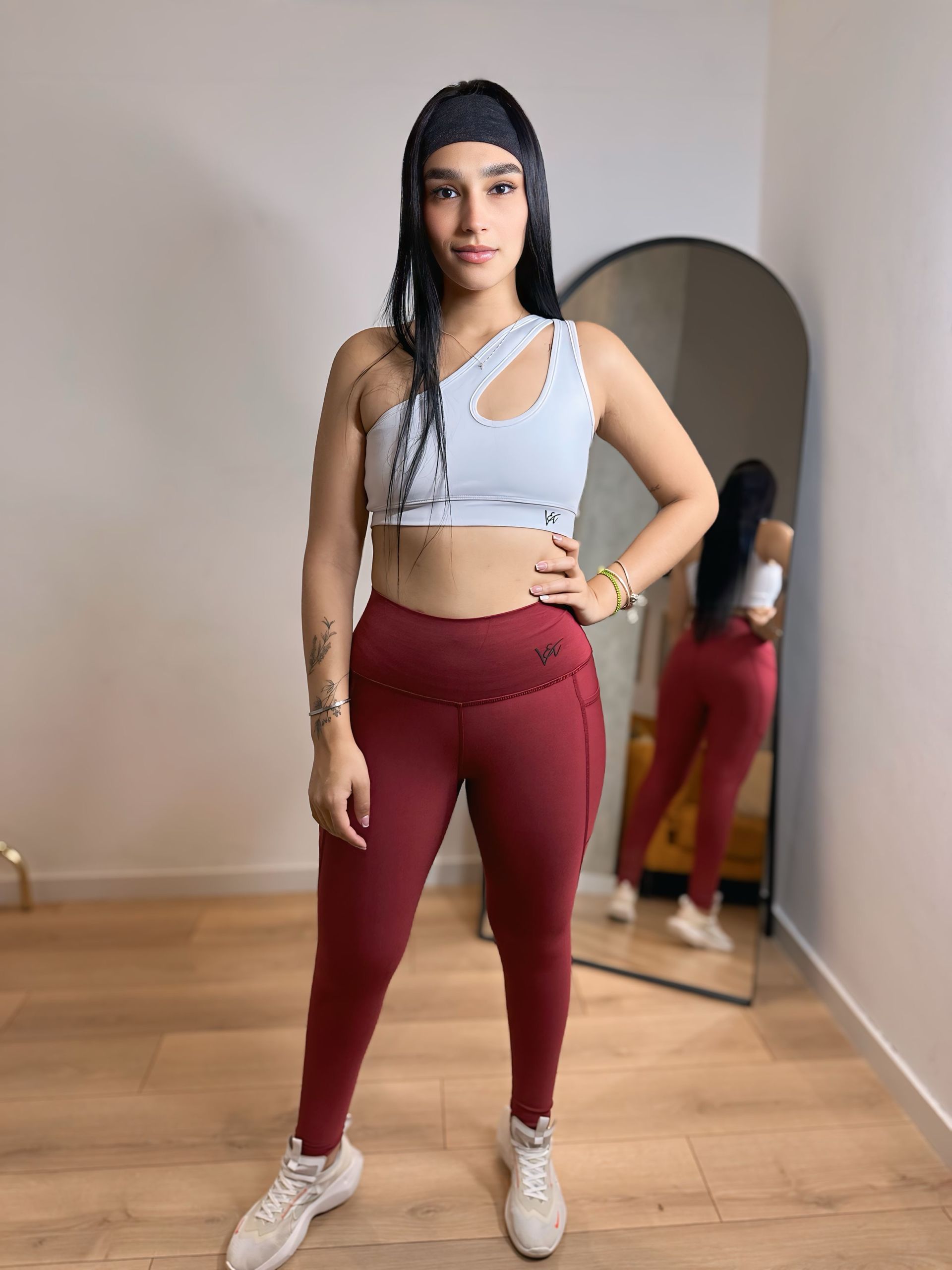 A woman in a white crop top and red leggings is standing in front of a mirror.