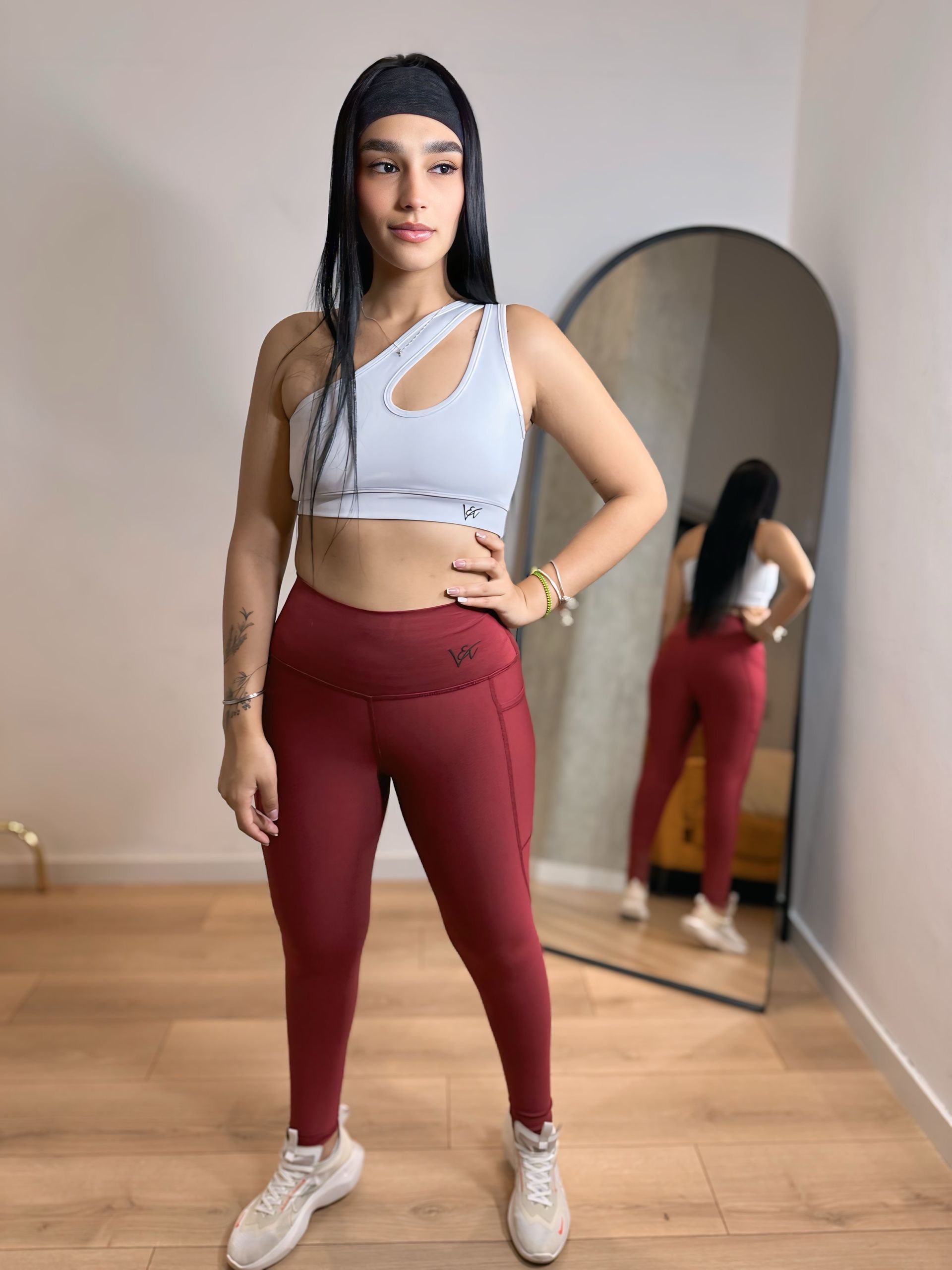 A woman in a white crop top and red leggings is standing in front of a mirror.