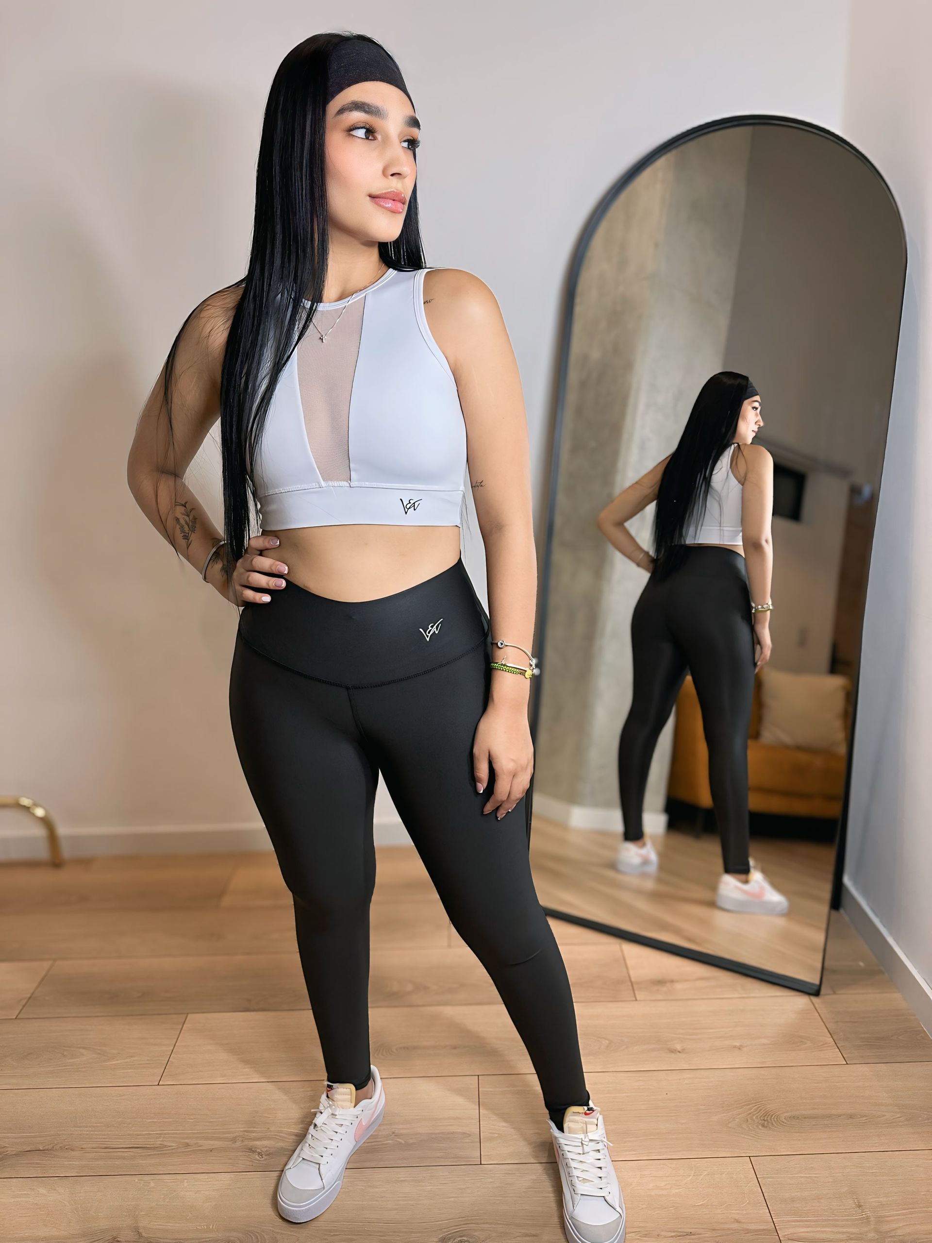 A woman is standing in front of a mirror wearing a crop top and leggings.