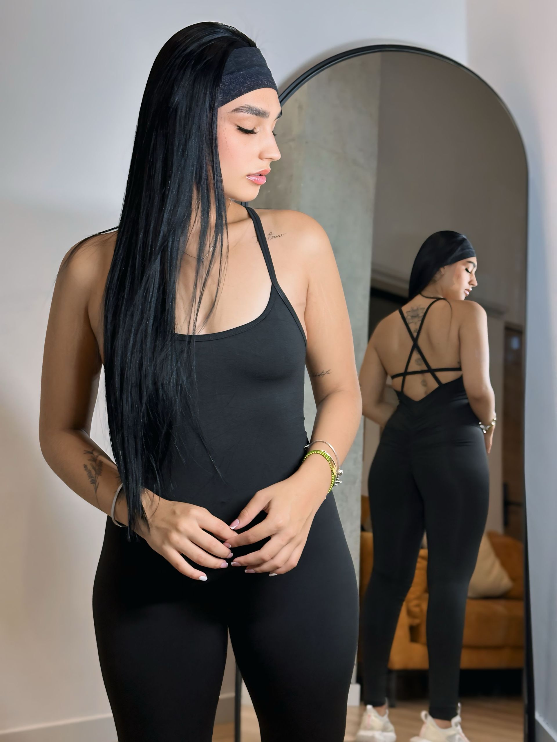 A woman in a black jumpsuit is standing in front of a mirror