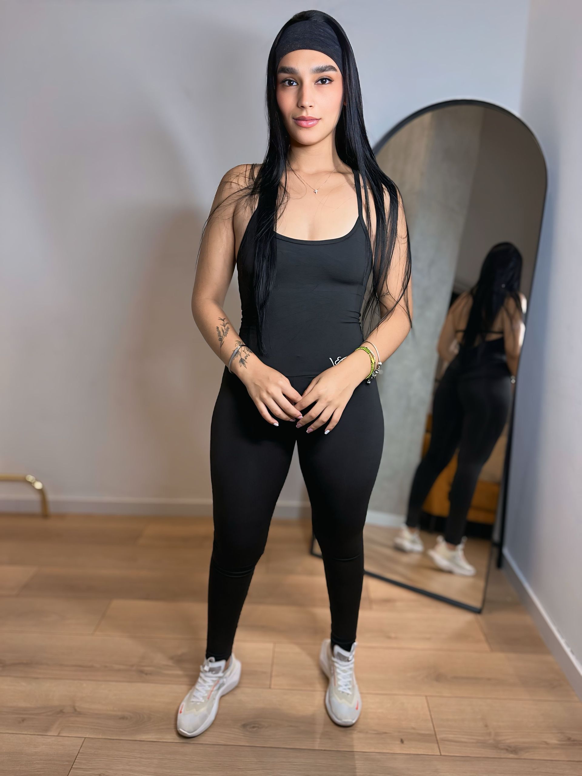 A woman in a black jumpsuit is standing in front of a mirror.