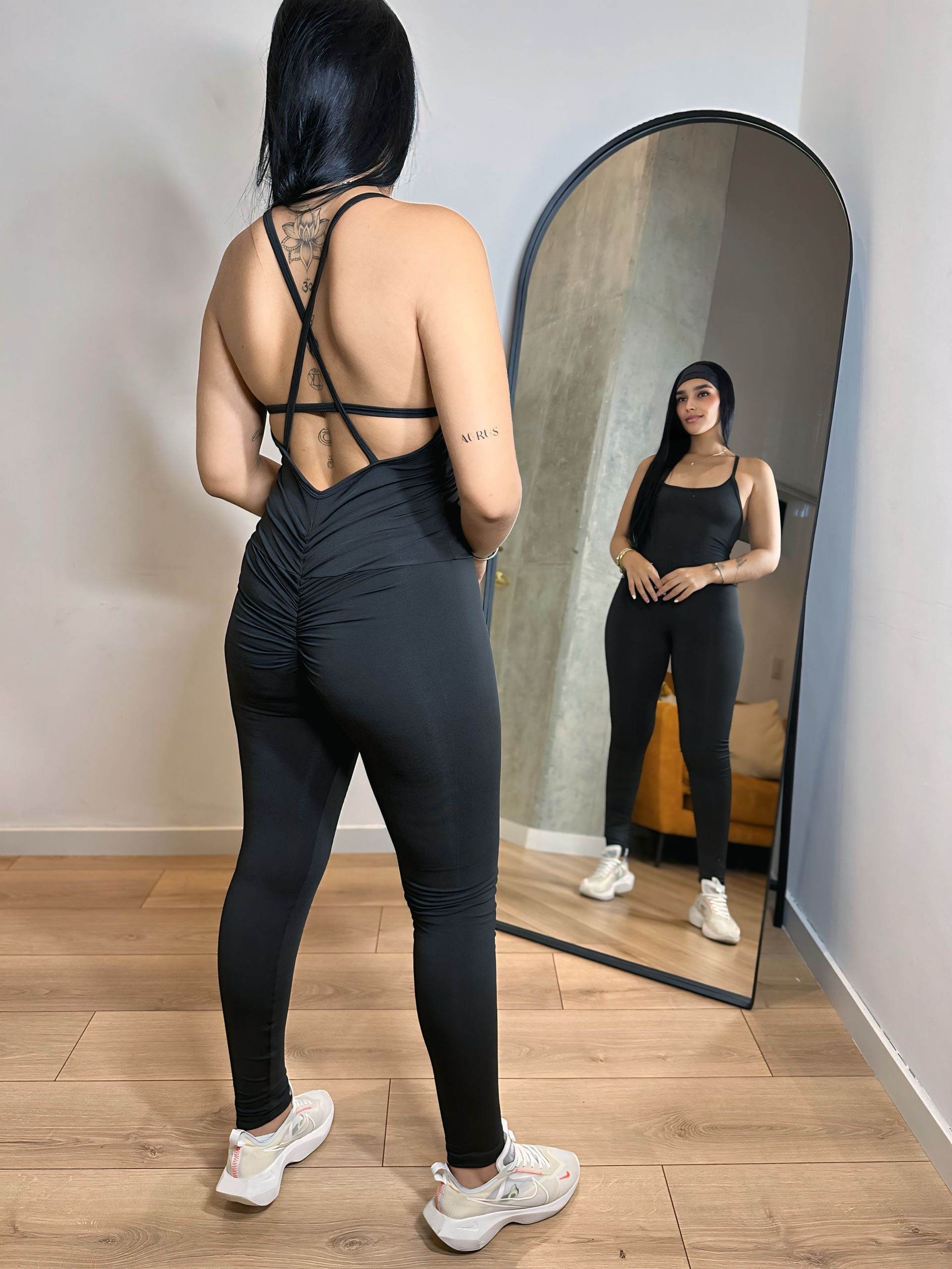 A woman in a black jumpsuit is standing in front of a mirror.