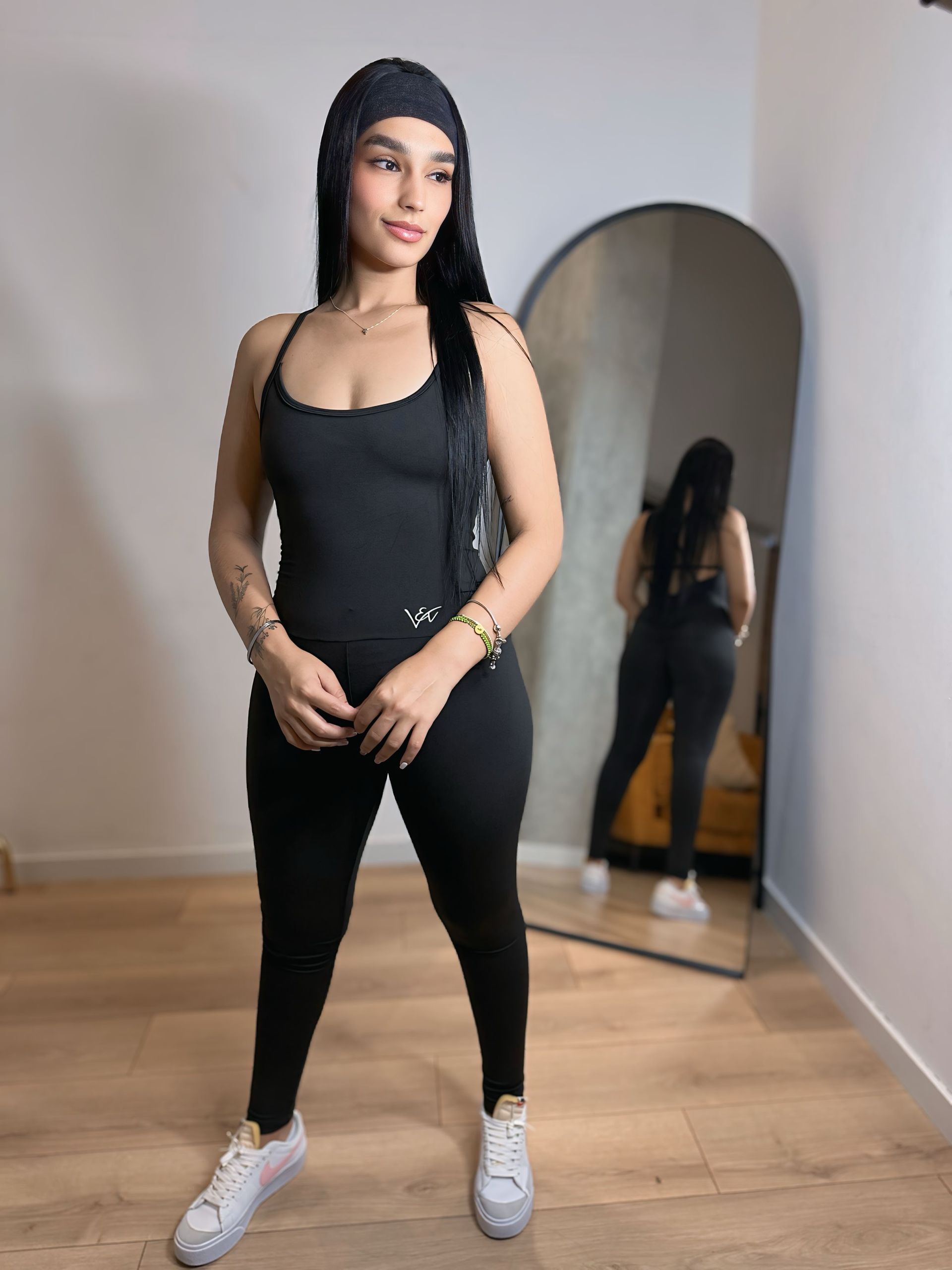 A woman in a black jumpsuit is standing in front of a mirror.