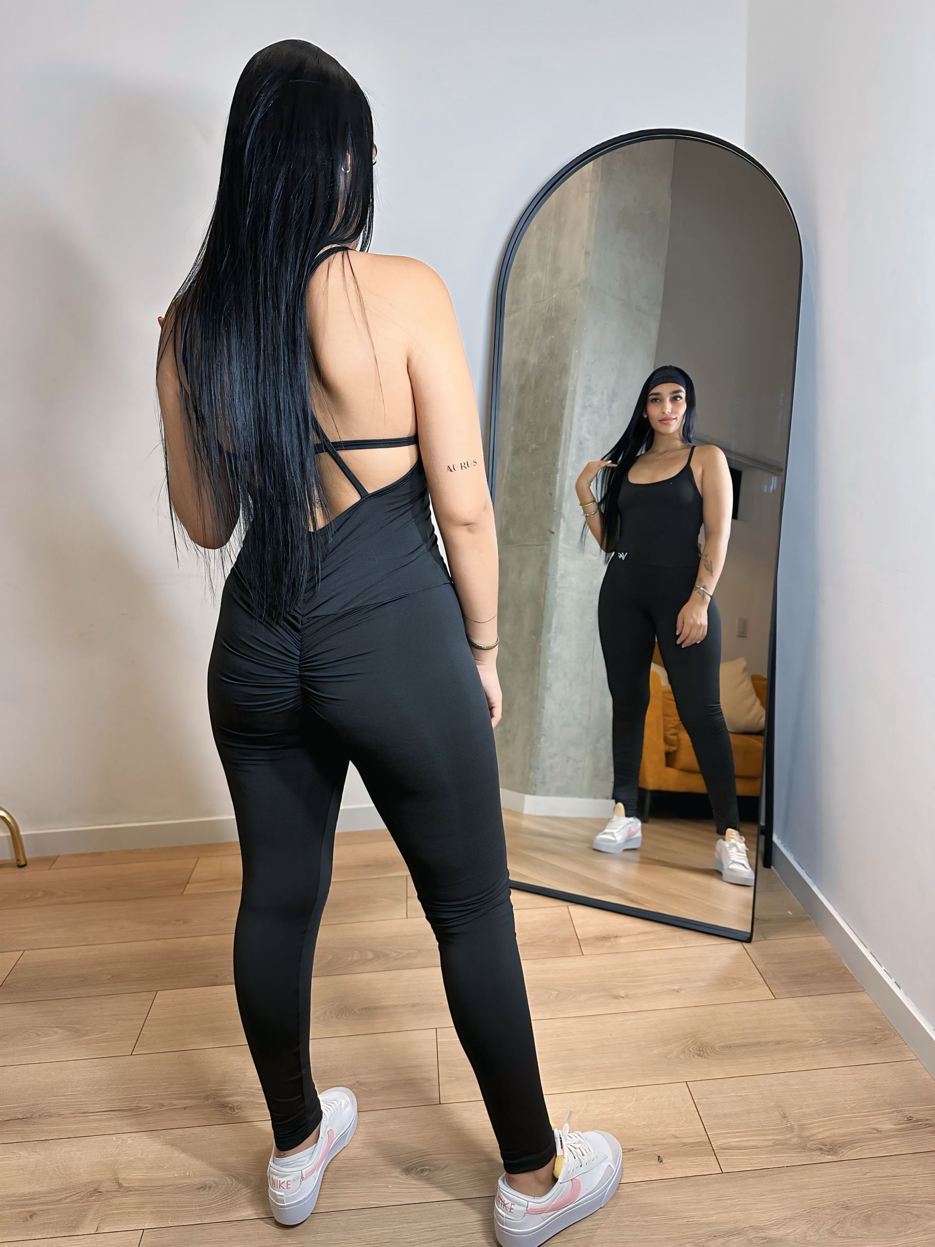A woman in a black jumpsuit is standing in front of a mirror.