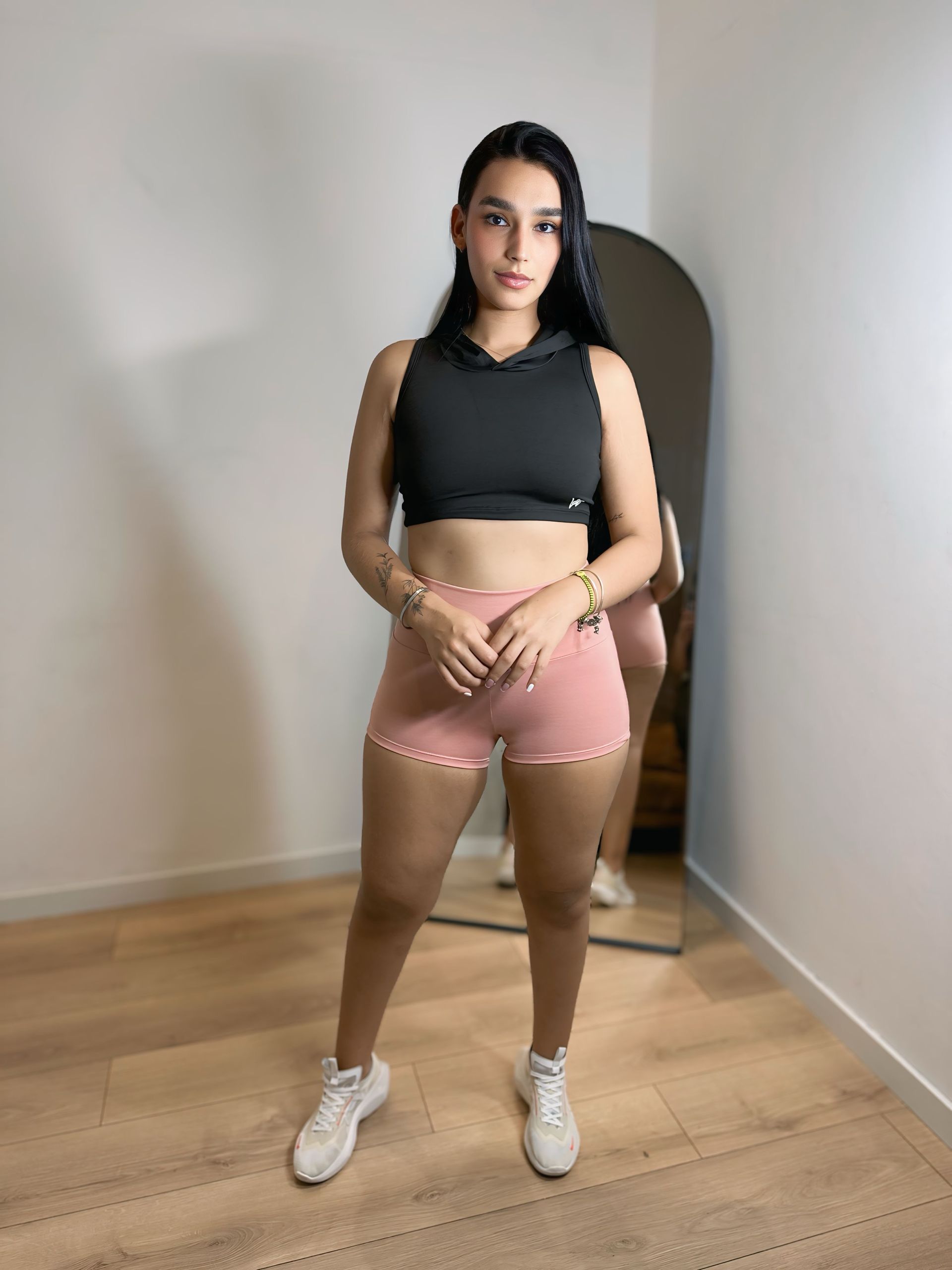A woman in a black crop top and pink shorts is standing in front of a mirror.