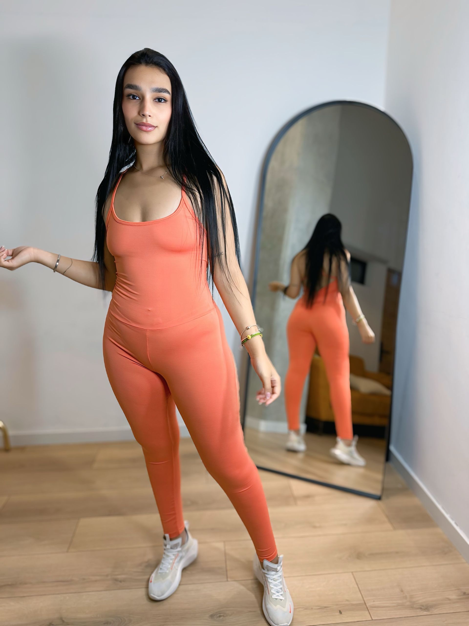 A woman in an orange jumpsuit is standing in front of a mirror.