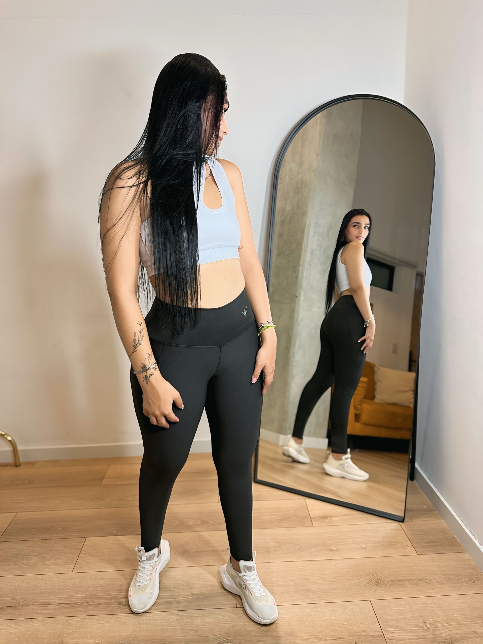 A woman is standing in front of a large mirror in a room.