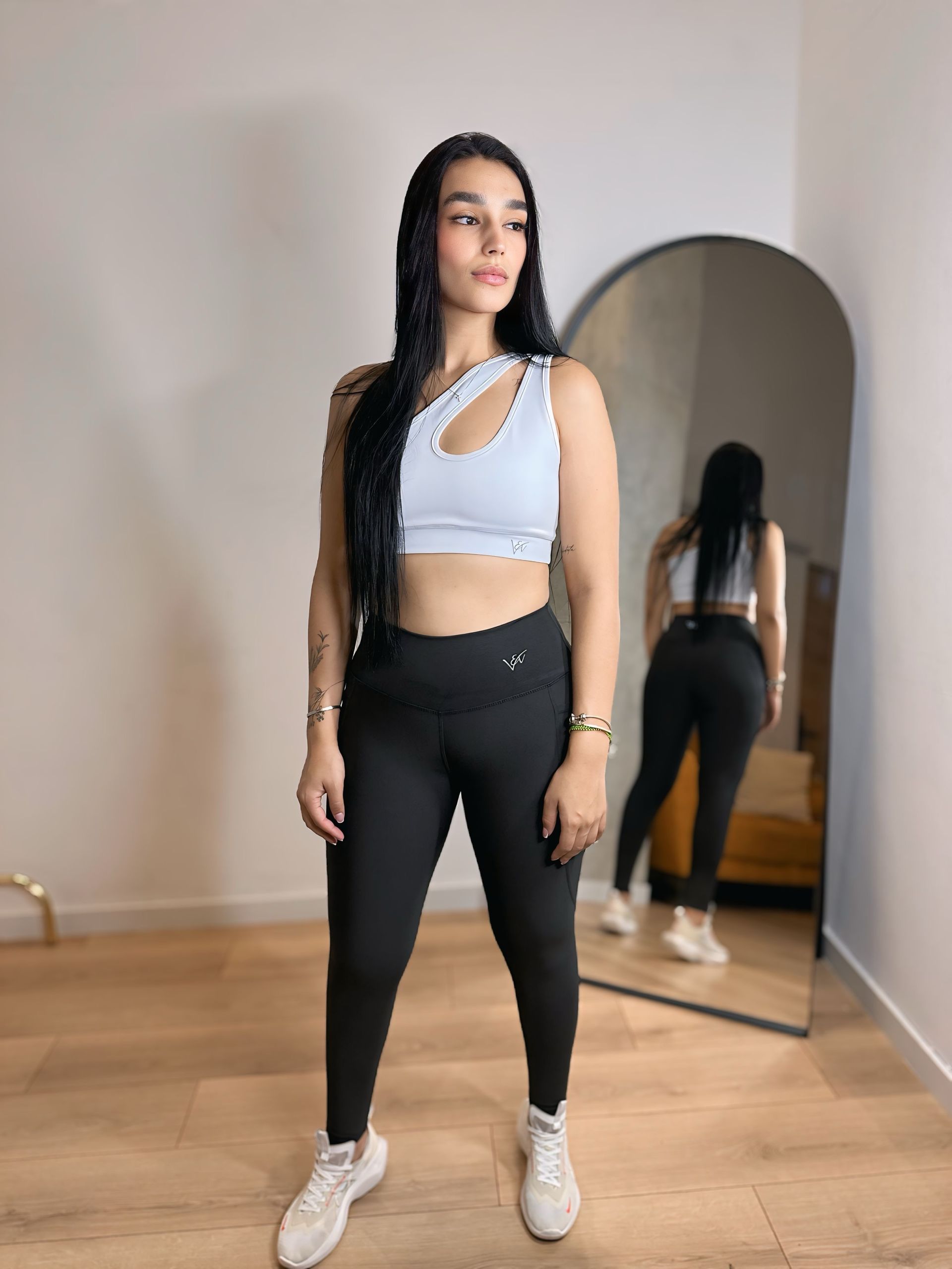 A woman is standing in front of a mirror wearing a crop top and leggings.