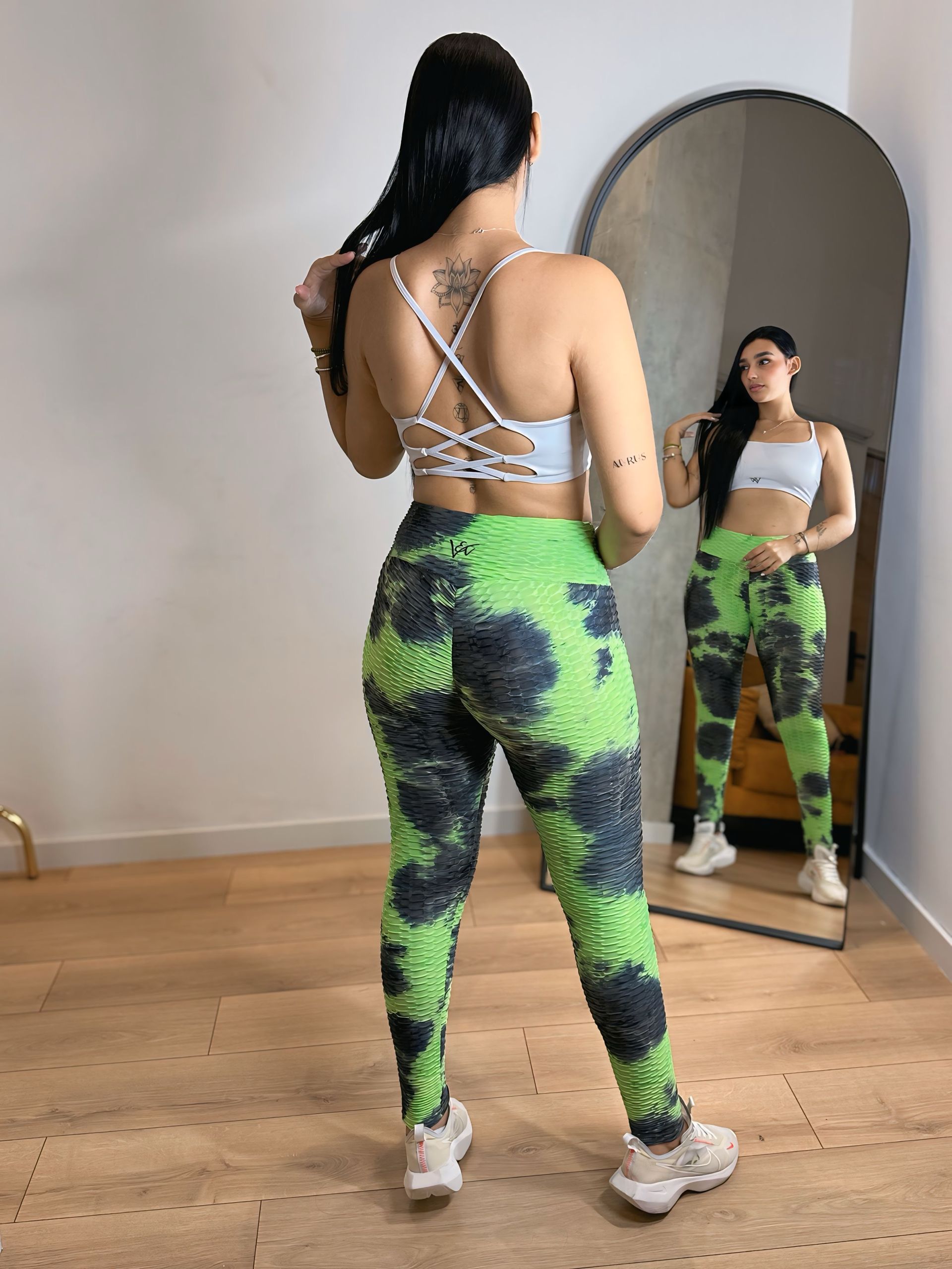 A woman is standing in front of a mirror wearing green tie dye leggings.
