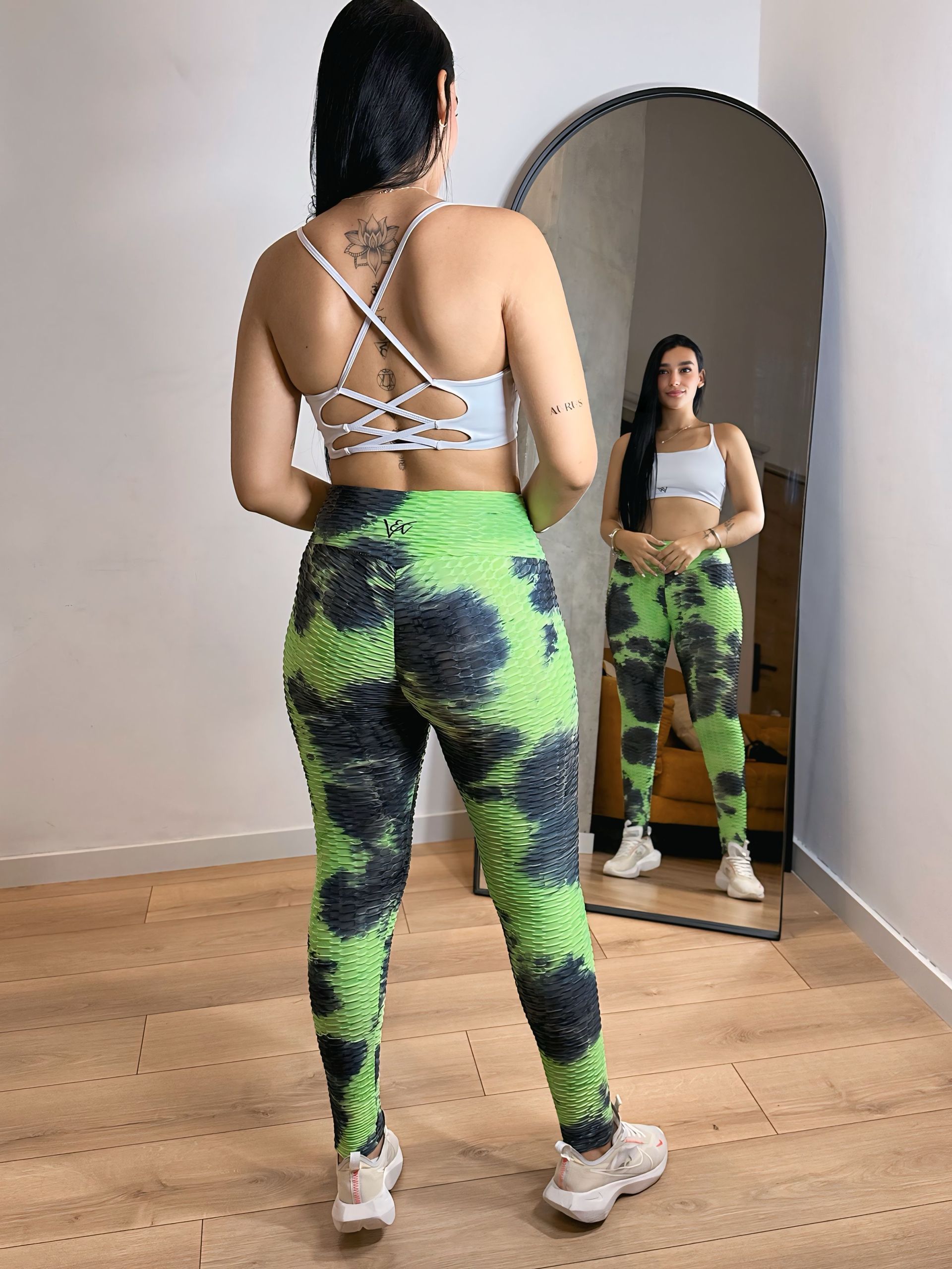 A woman is standing in front of a mirror wearing green tie dye leggings.