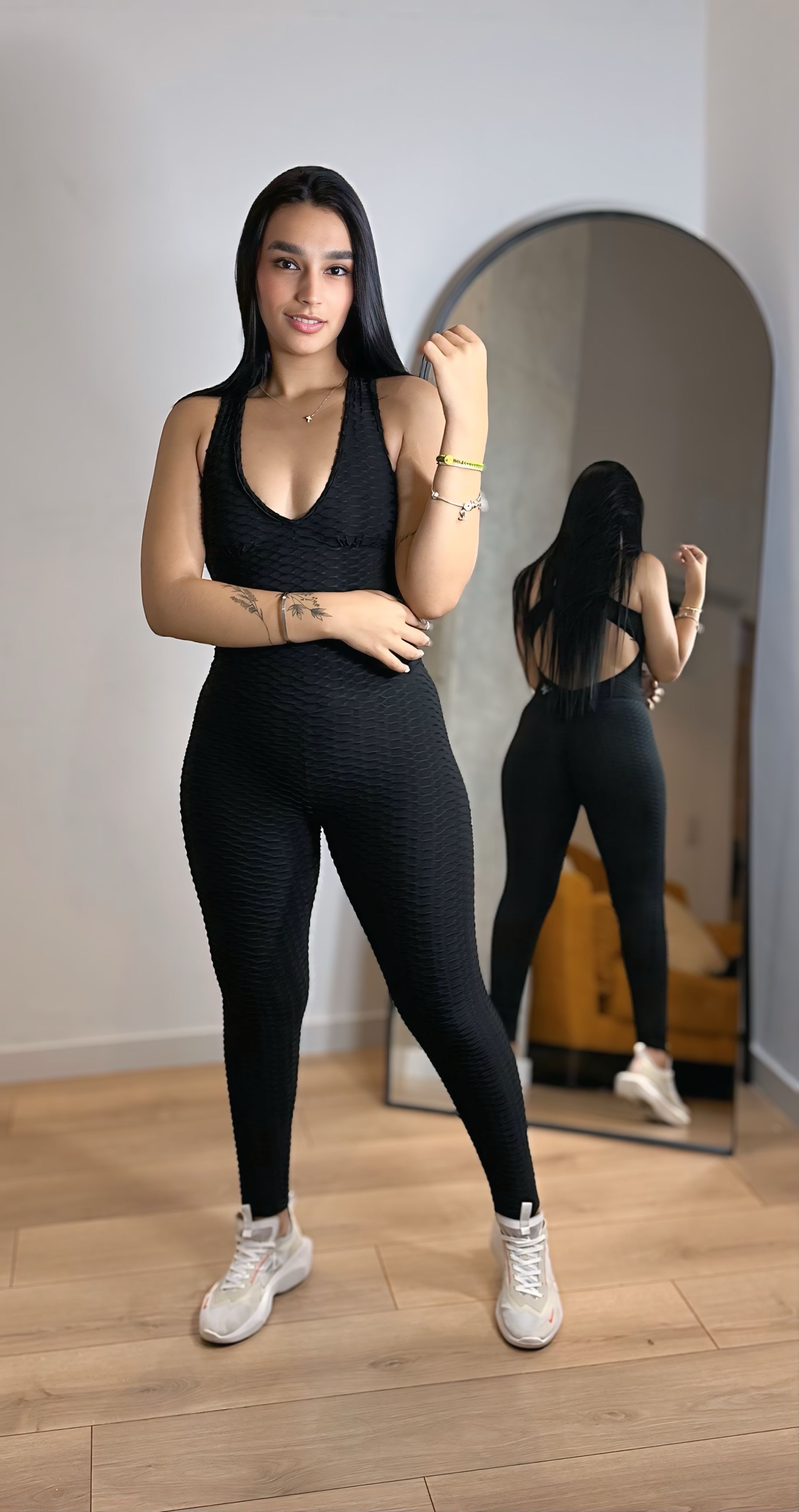 A woman in a black jumpsuit is standing in front of a mirror.