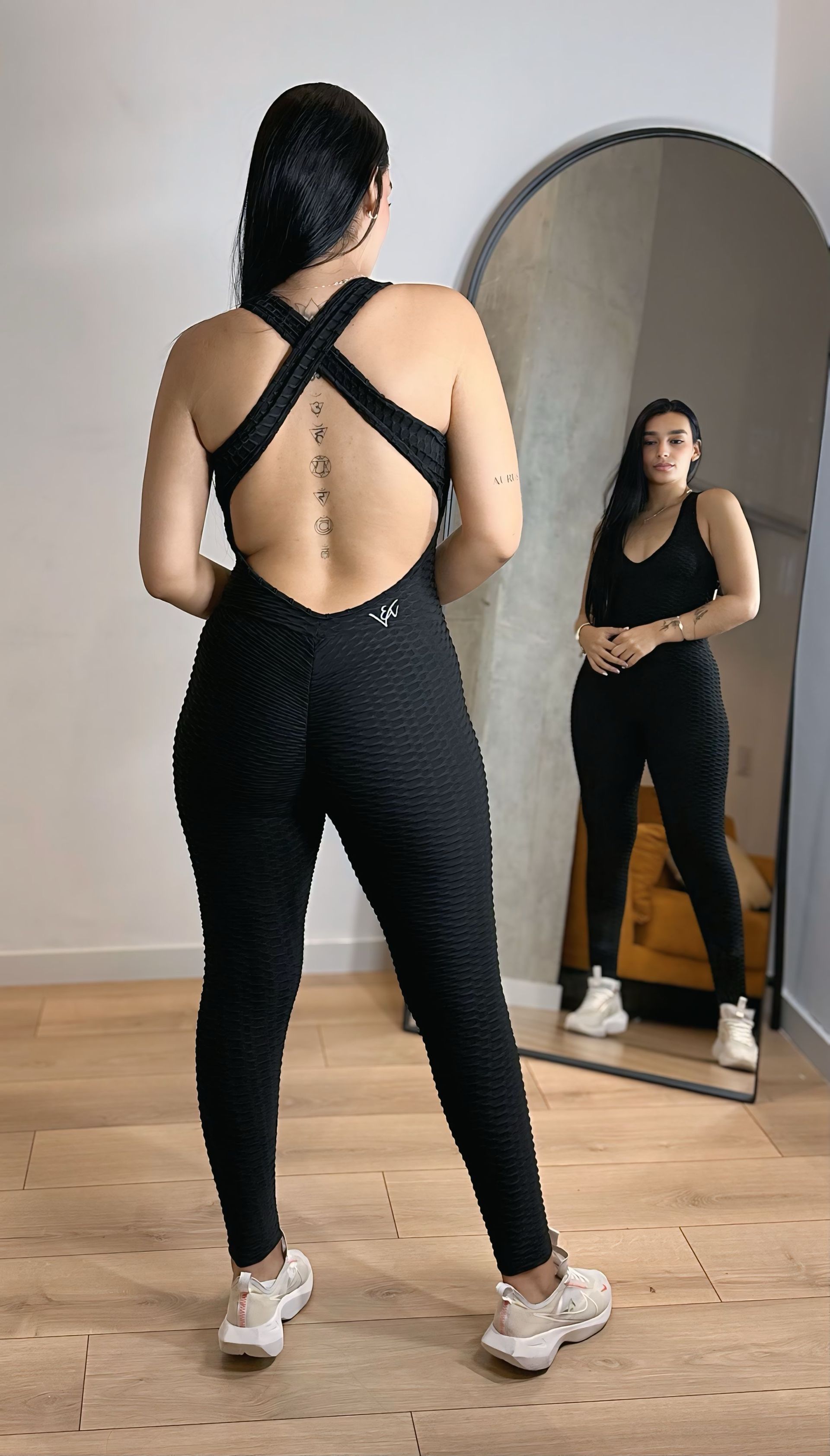 A woman in a black jumpsuit is standing in front of a mirror.