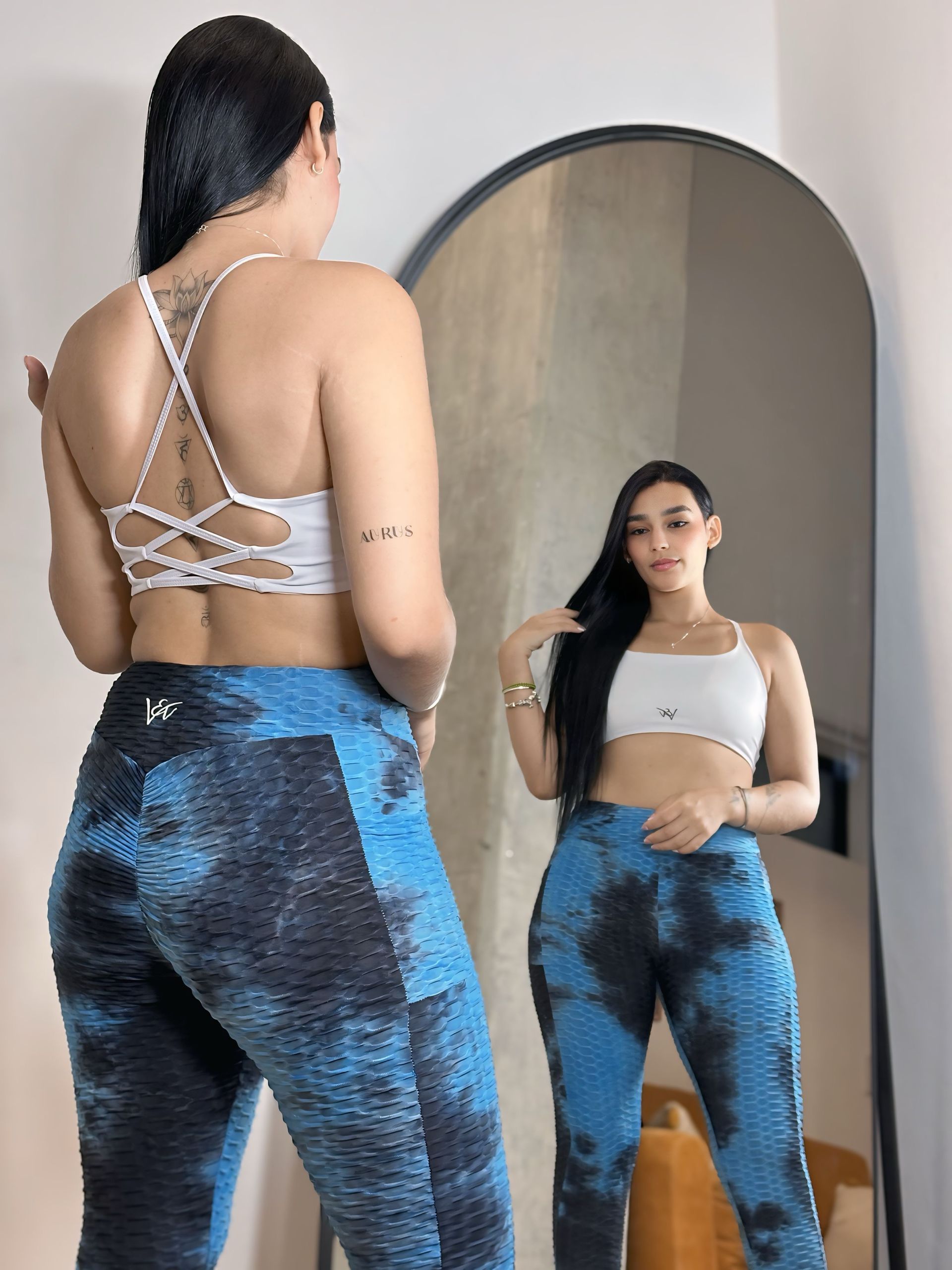 A woman is standing in front of a mirror wearing blue leggings and a white top.