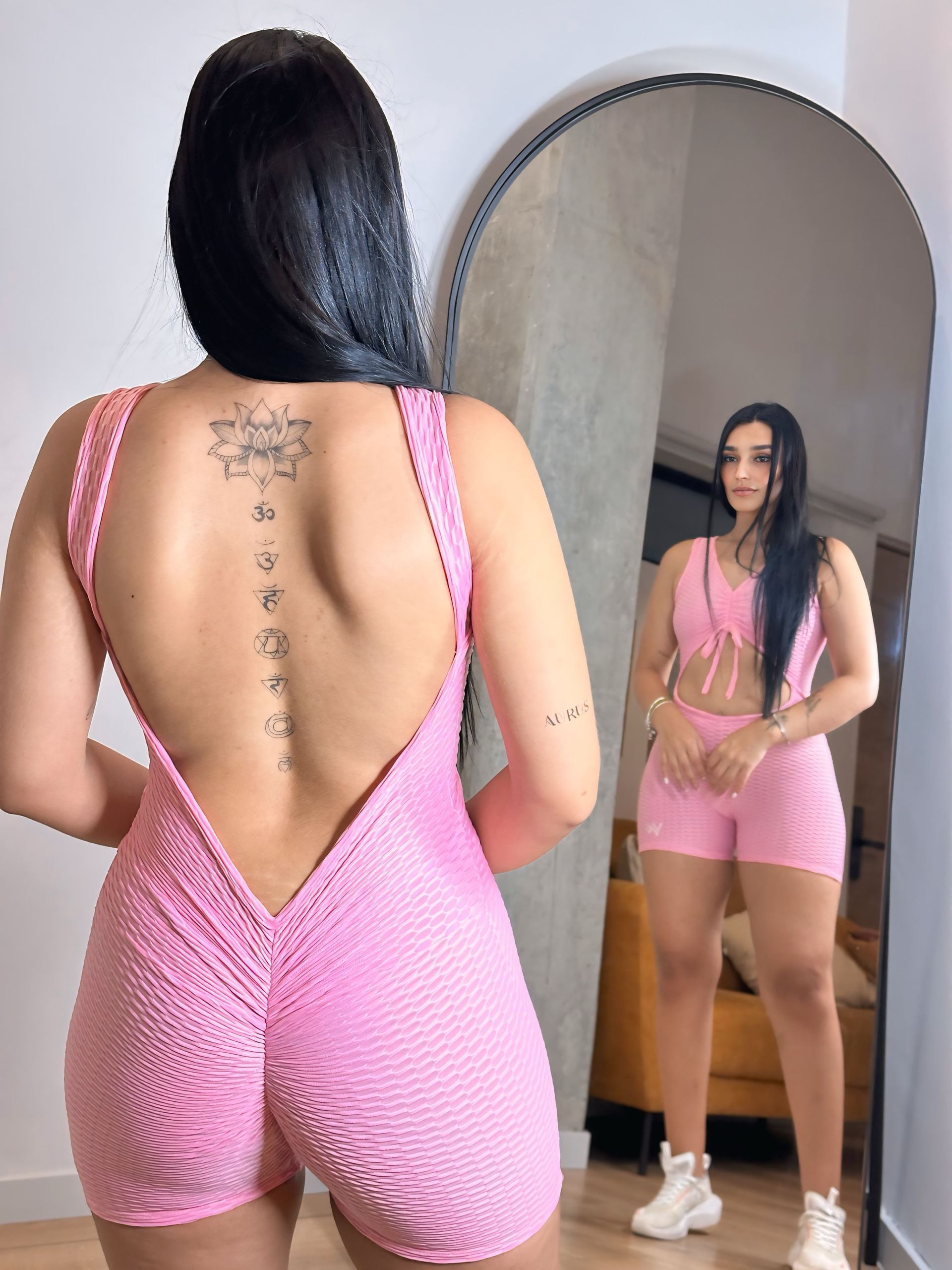 A woman in a pink jumpsuit is standing in front of a mirror.