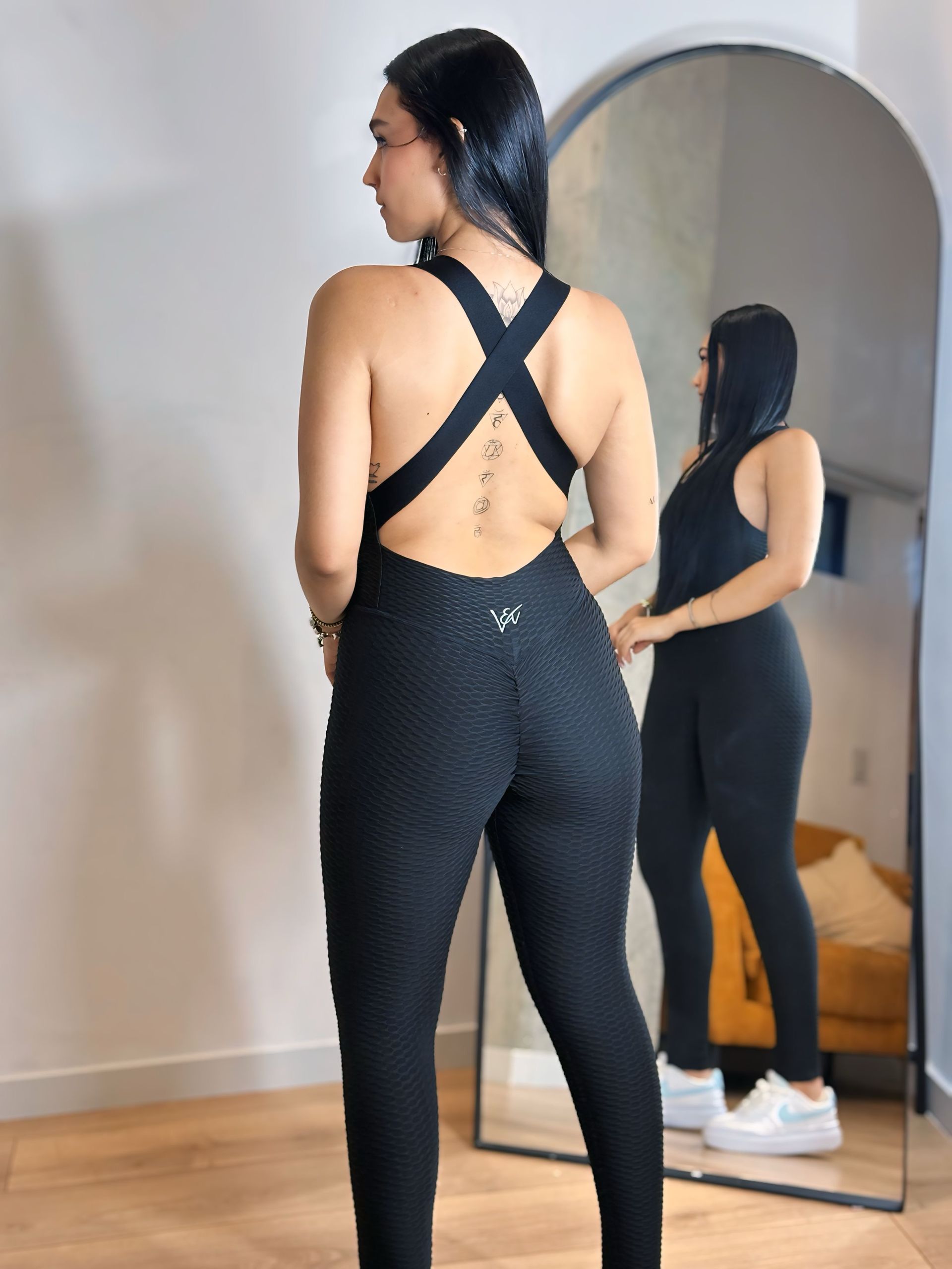 A woman in a black jumpsuit is standing in front of a mirror.