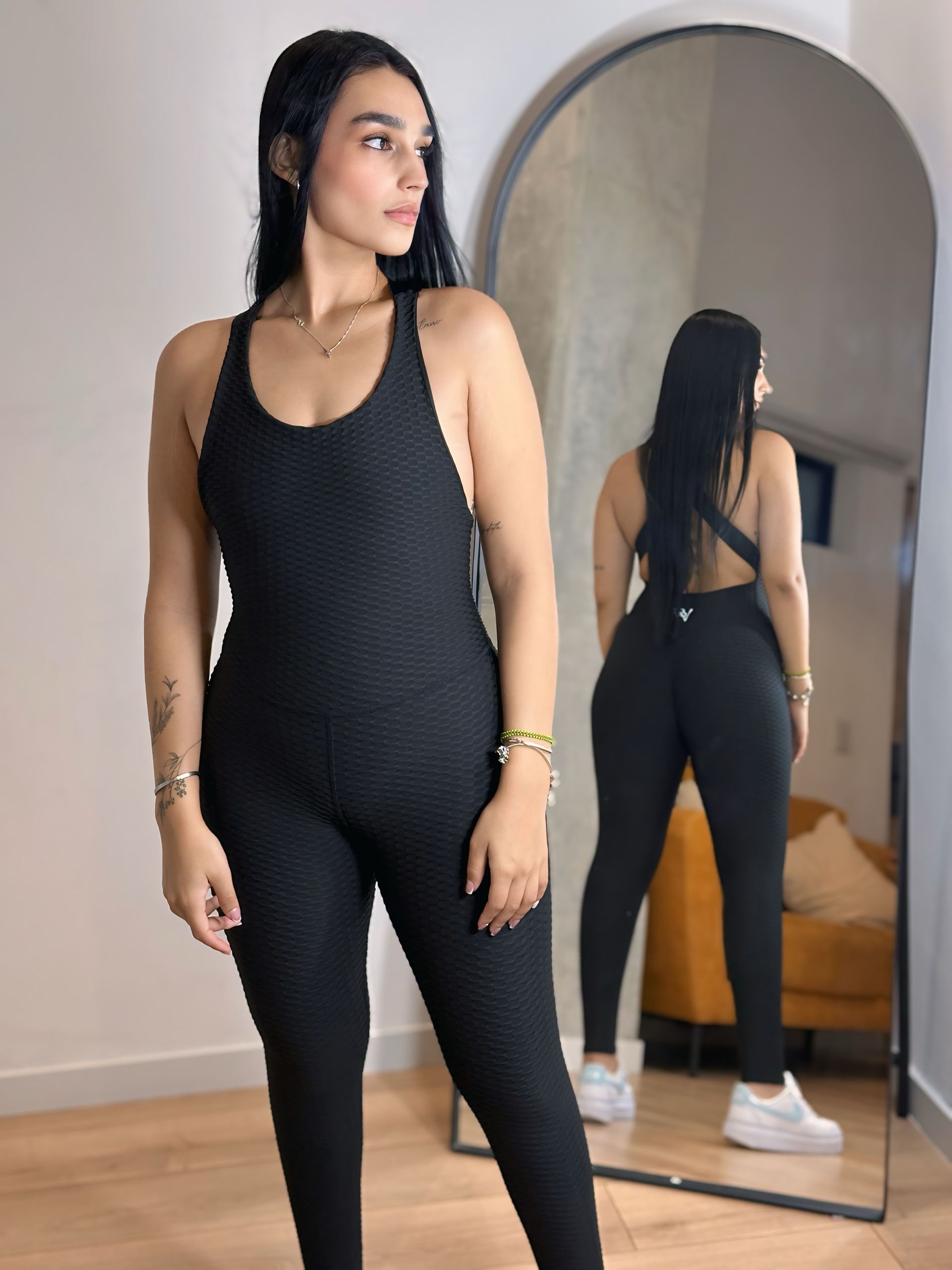 A woman in a black jumpsuit is standing in front of a mirror.