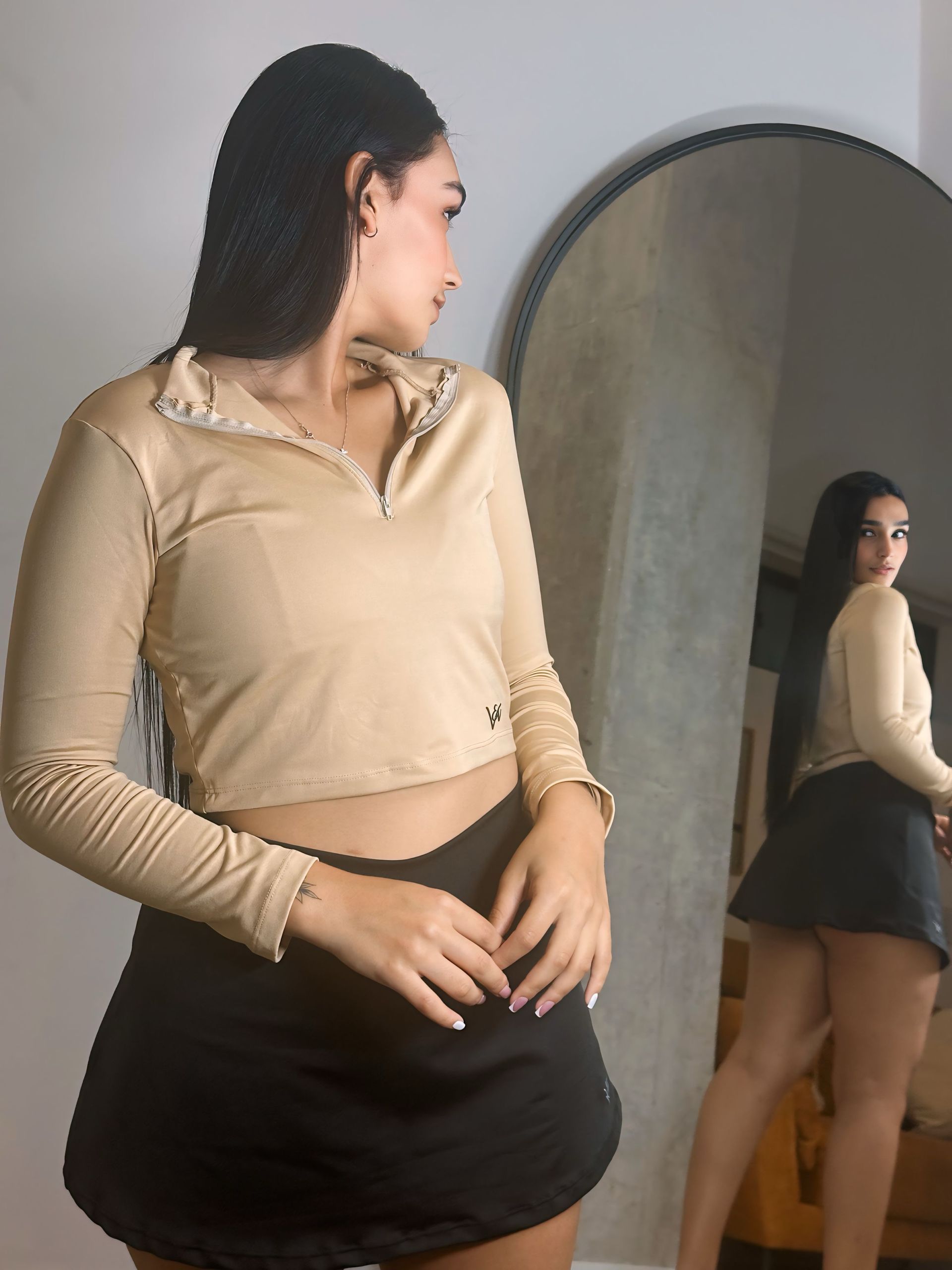A woman in a crop top and black skirt is standing in front of a mirror.