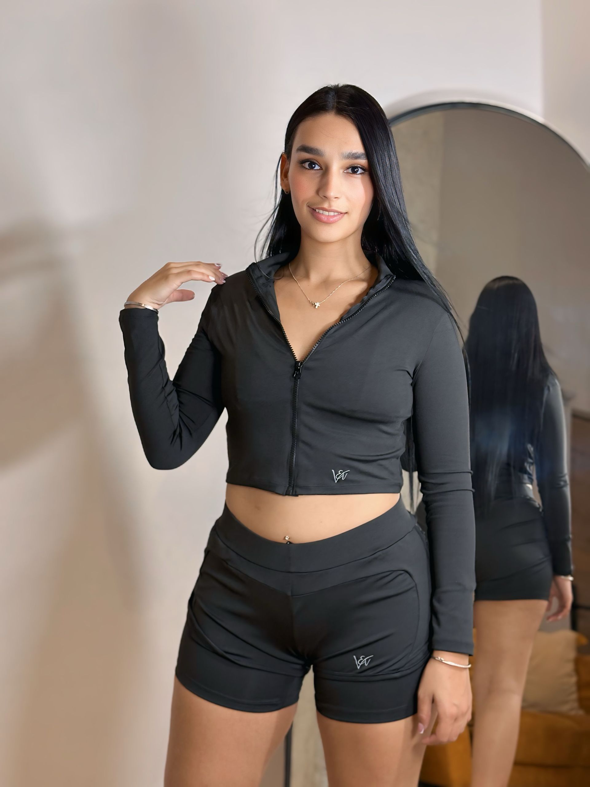A woman in a black crop top and shorts is standing in front of a mirror.