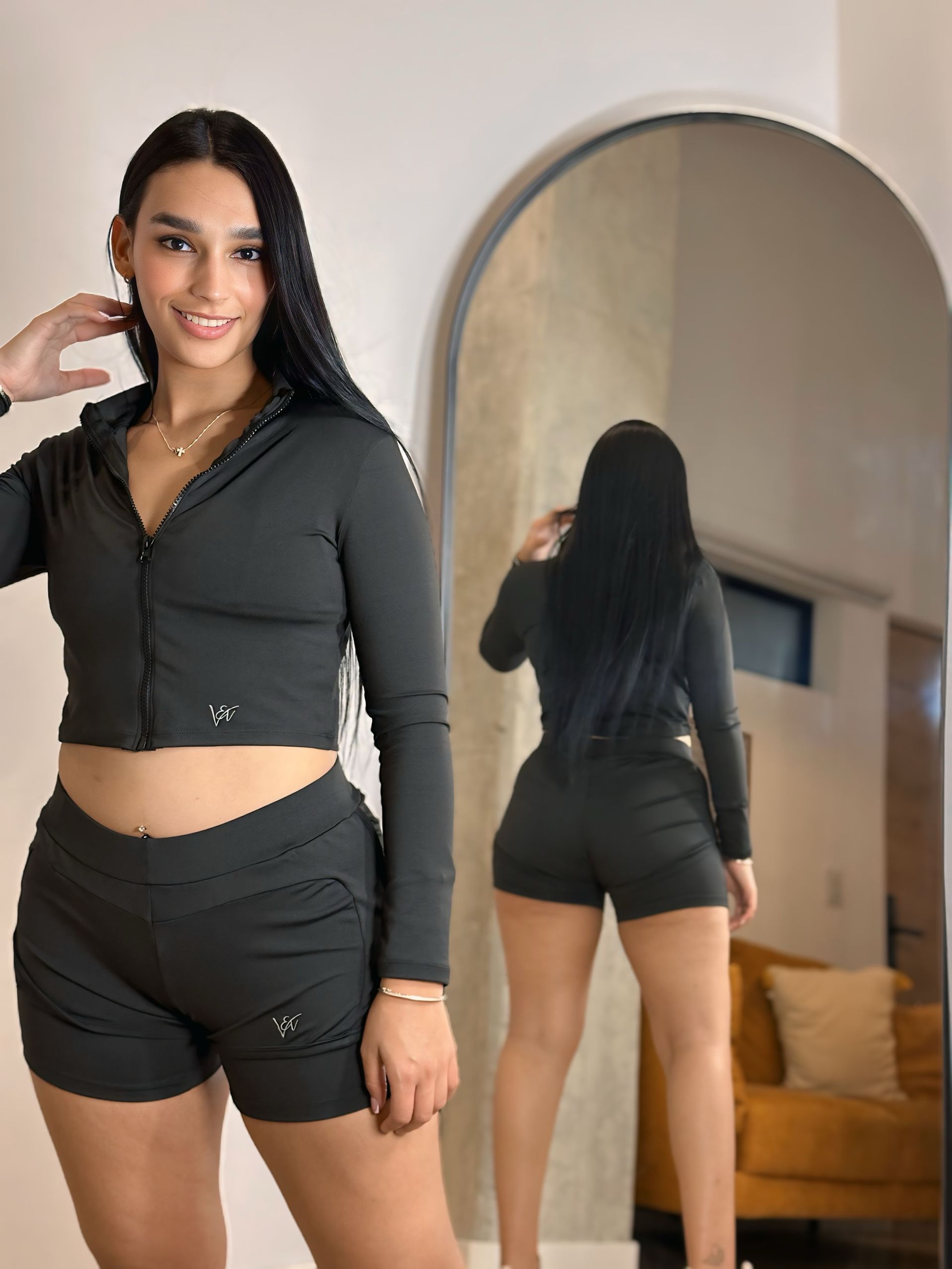 A woman in a crop top and shorts is standing in front of a mirror.