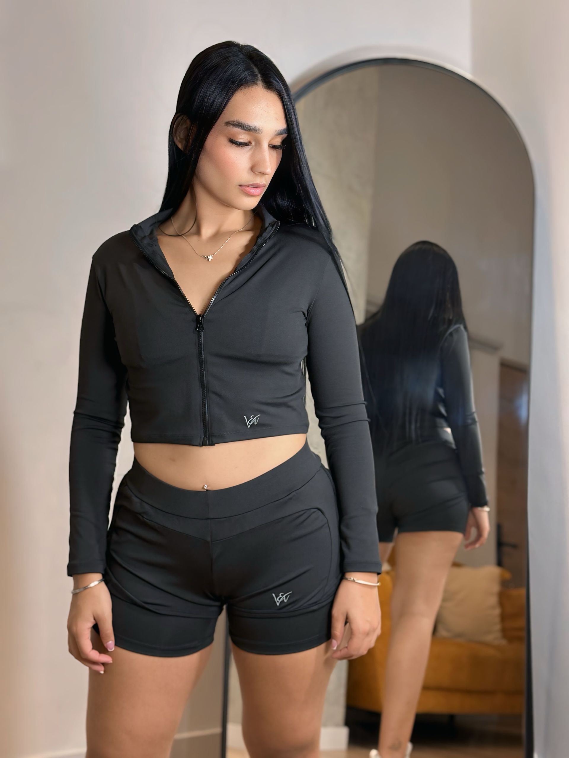 A woman in a black crop top and shorts is standing in front of a mirror.