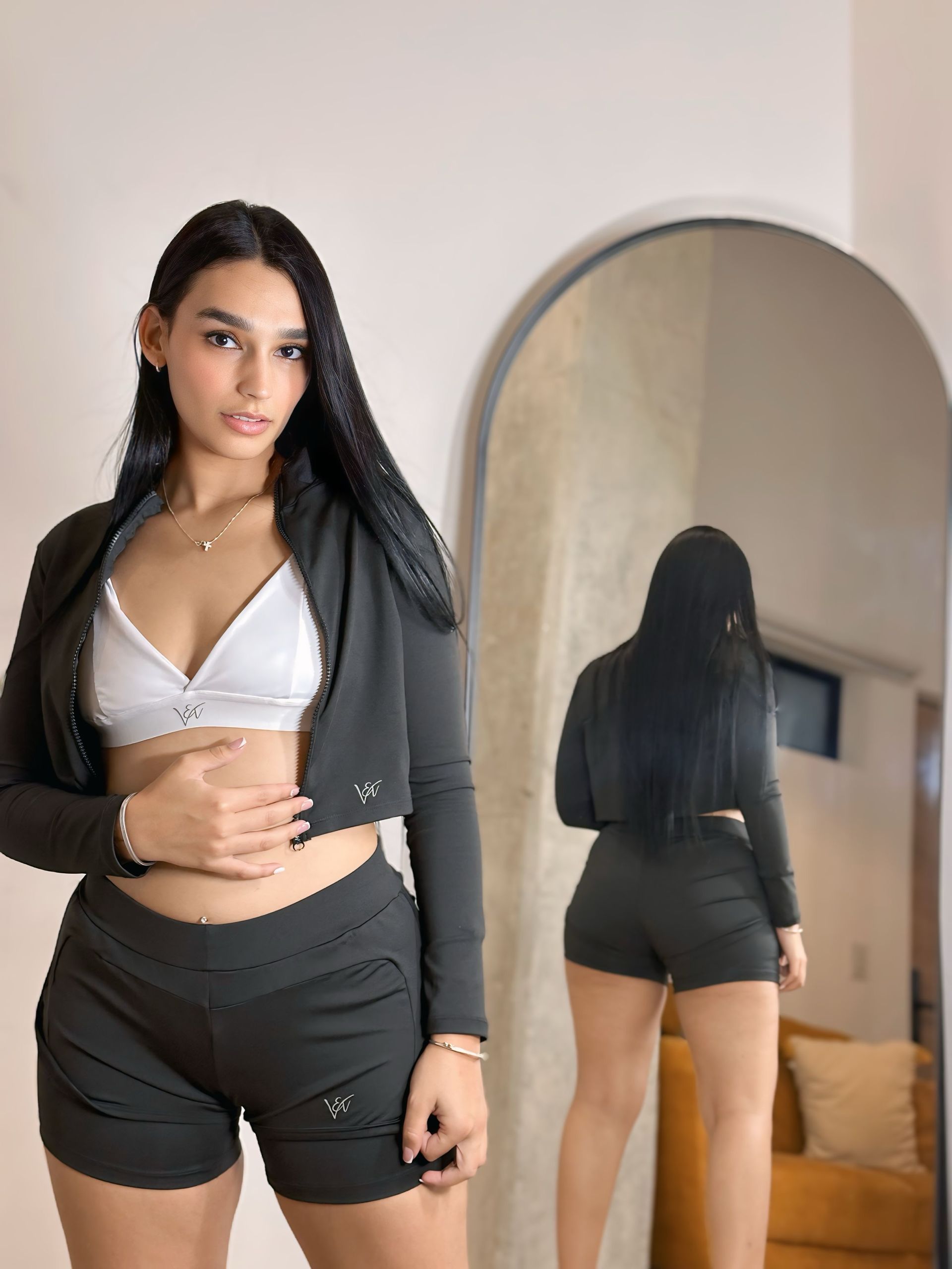 A woman in a crop top and shorts is standing in front of a mirror.