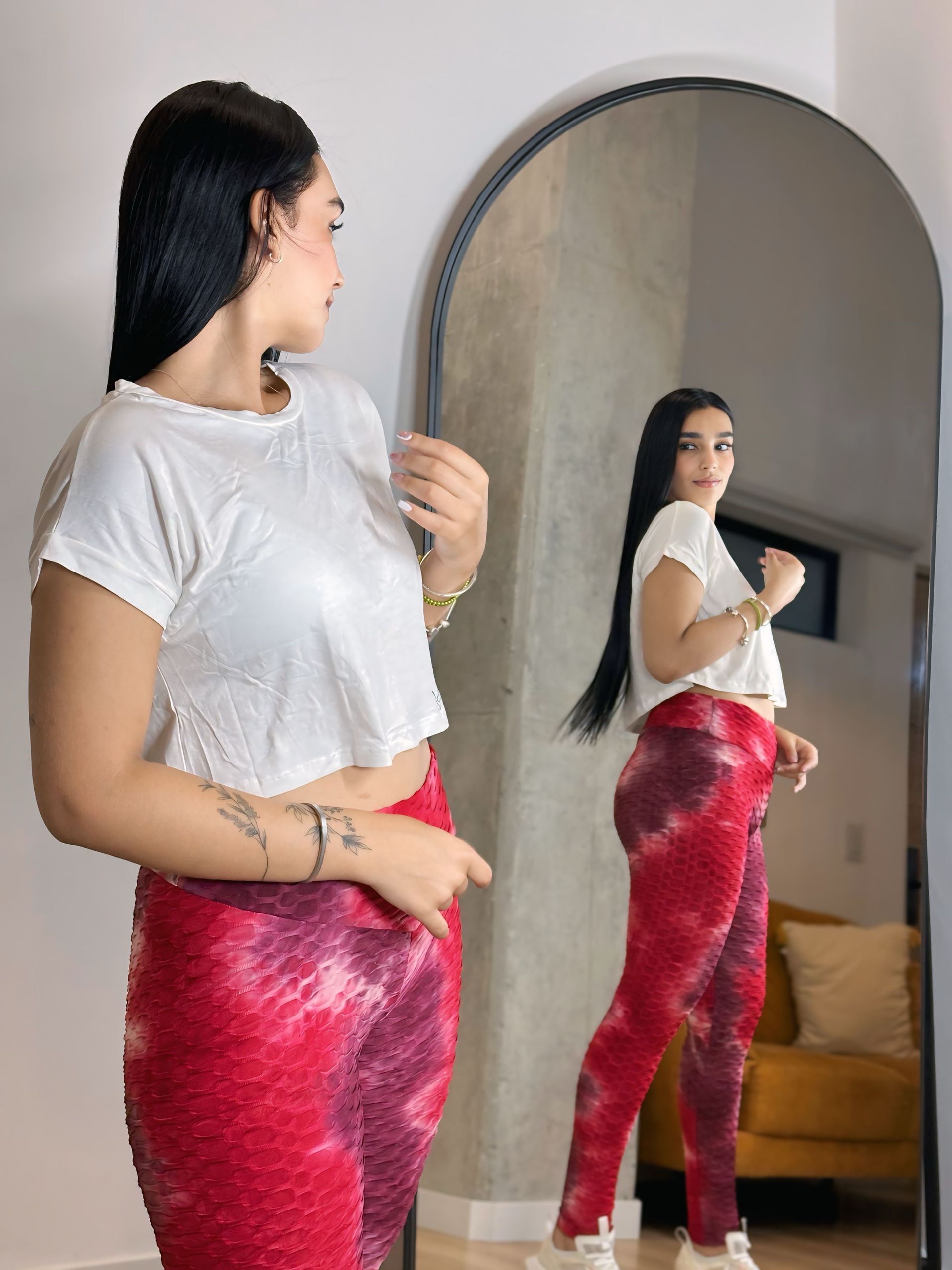 A woman in a white shirt and red pants is standing in front of a mirror.