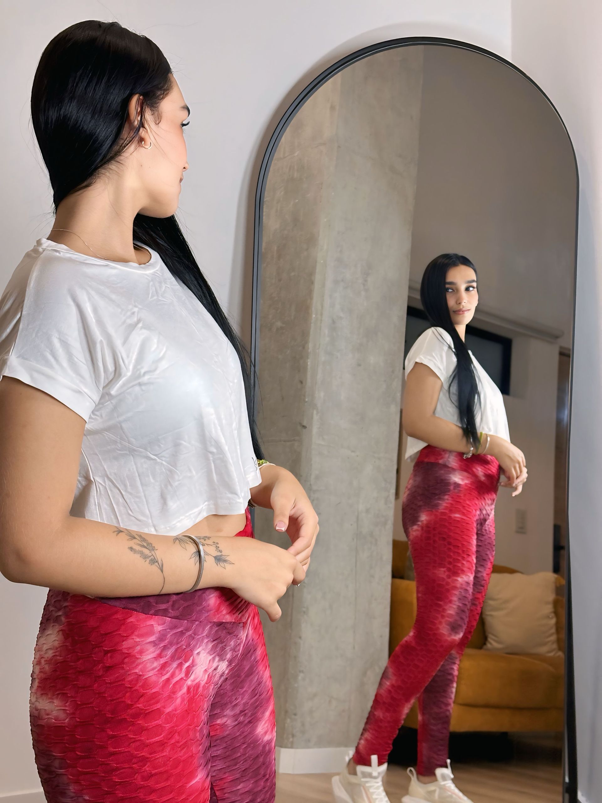 A woman in a white shirt and red pants is standing in front of a mirror.