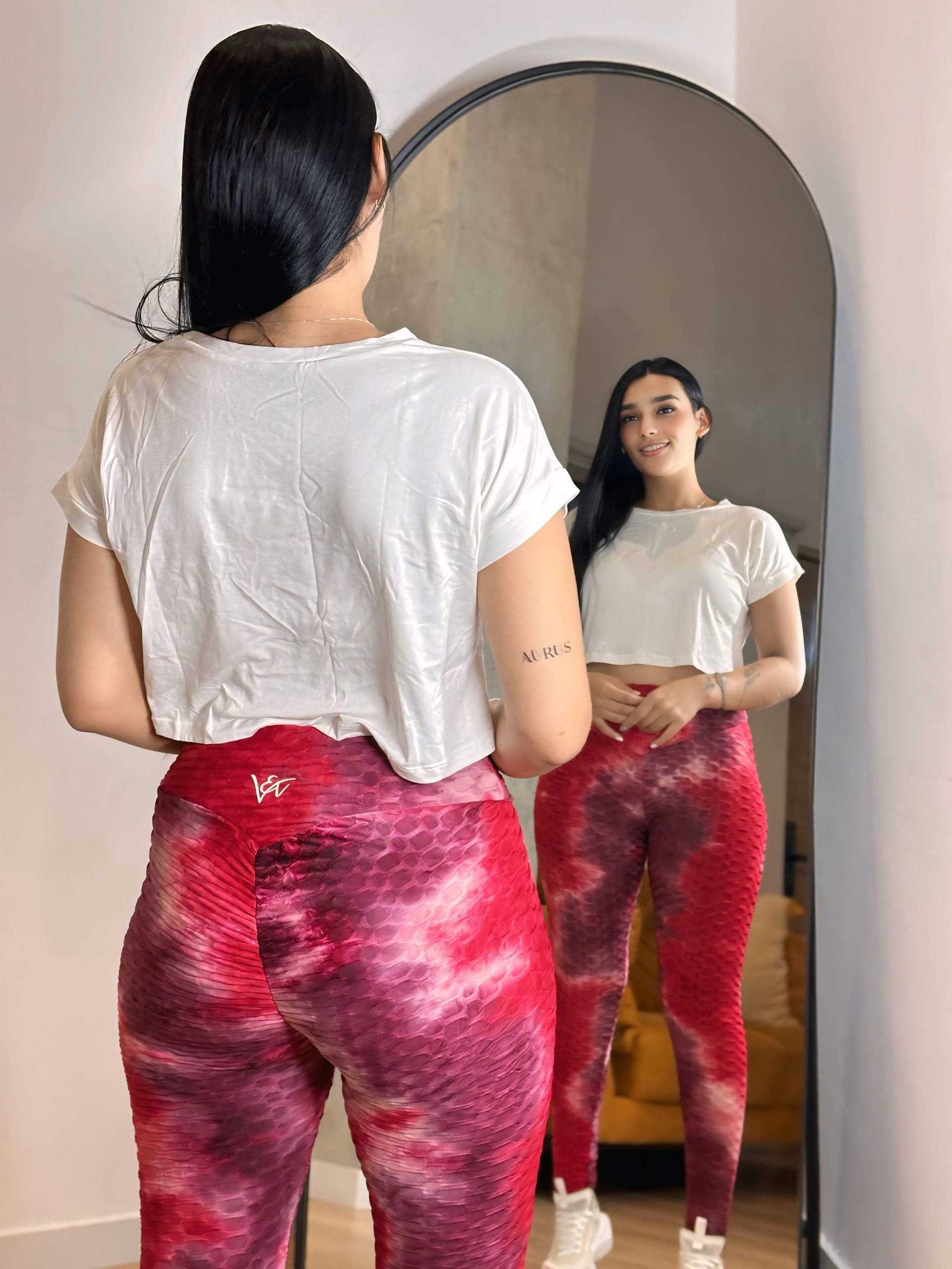 A woman in a white shirt and red pants is standing in front of a mirror.