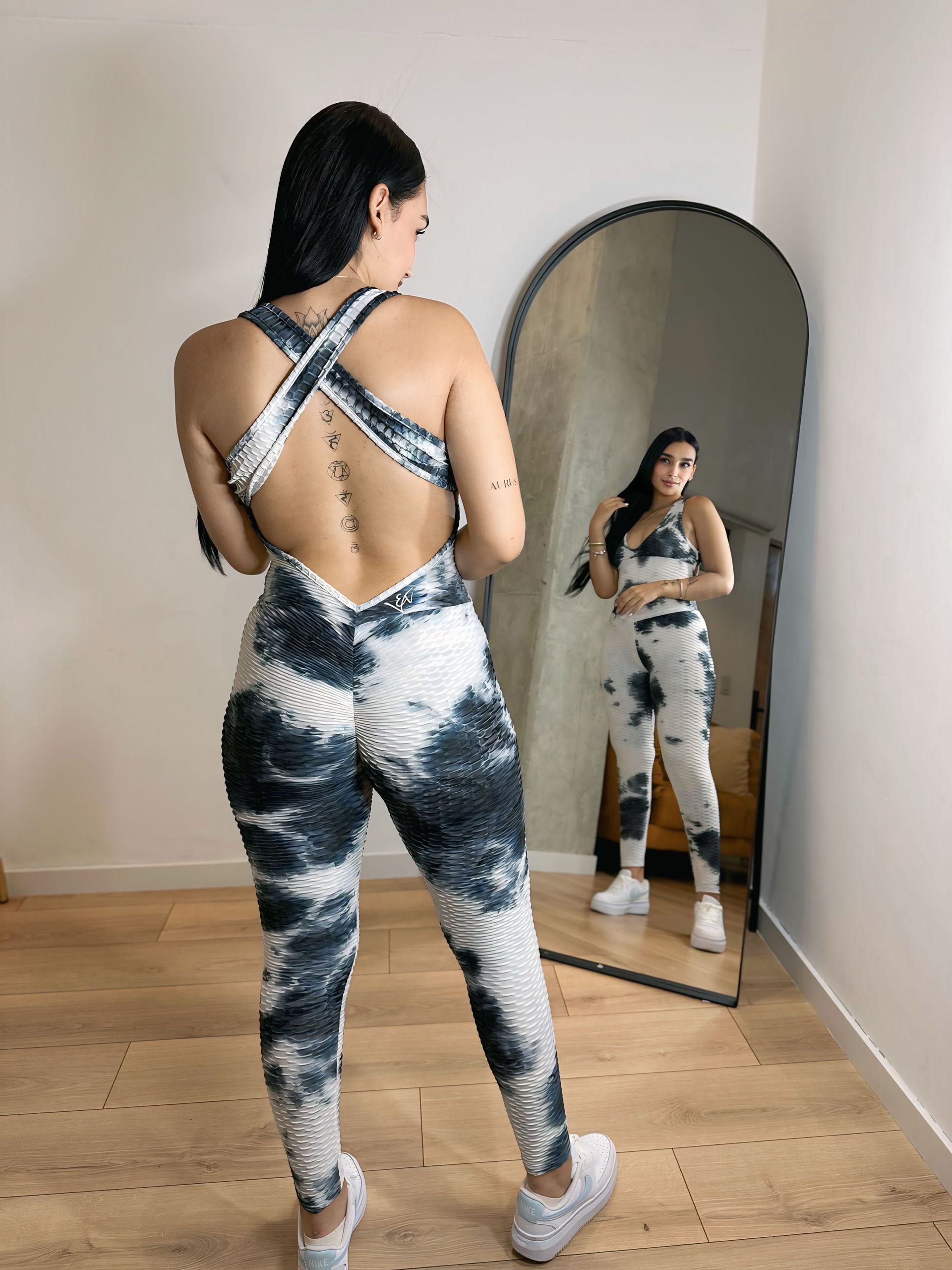 A woman is standing in front of a mirror wearing a tie dye jumpsuit.