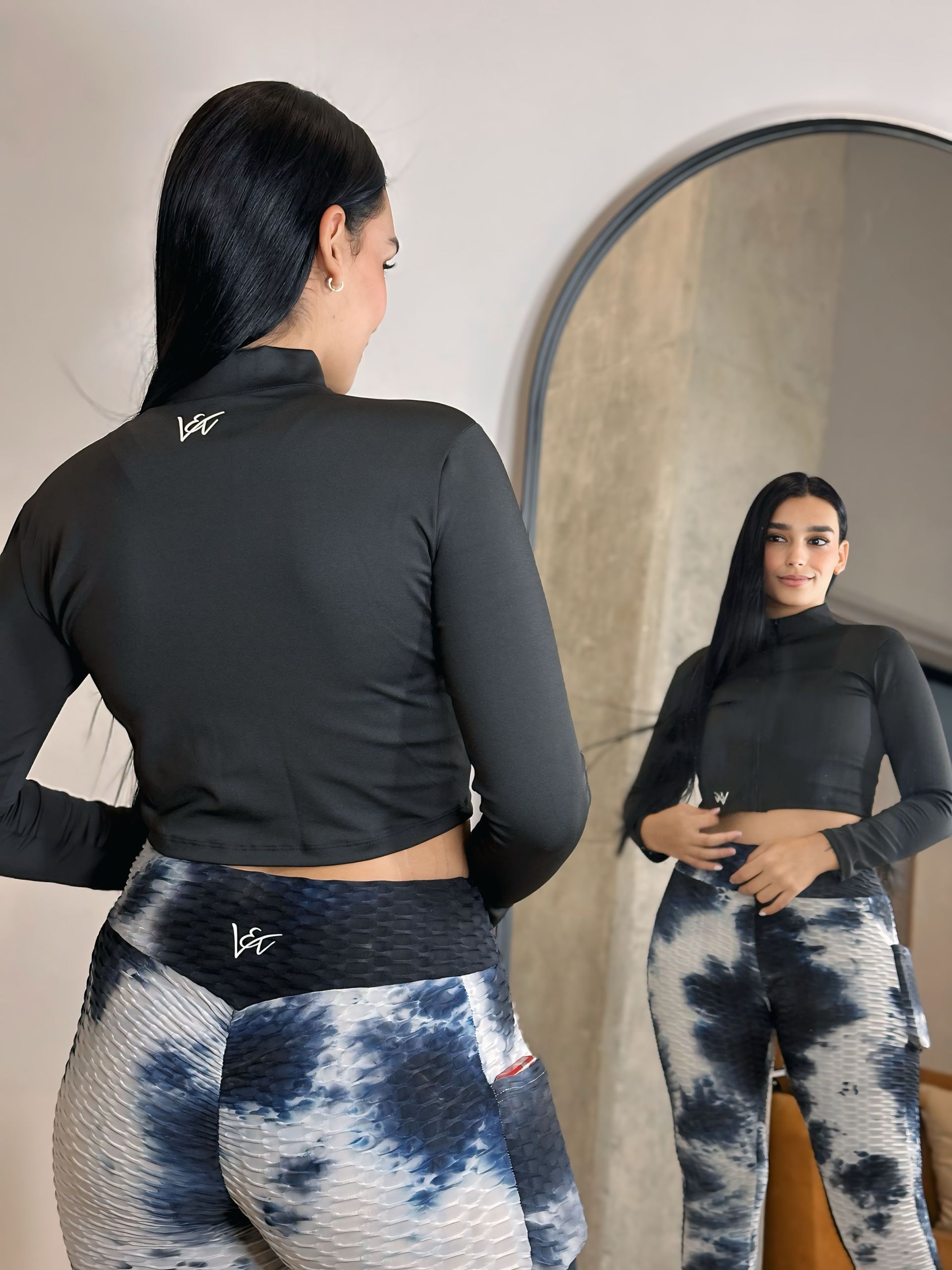 A woman is standing in front of a mirror wearing a black crop top and tie dye leggings.