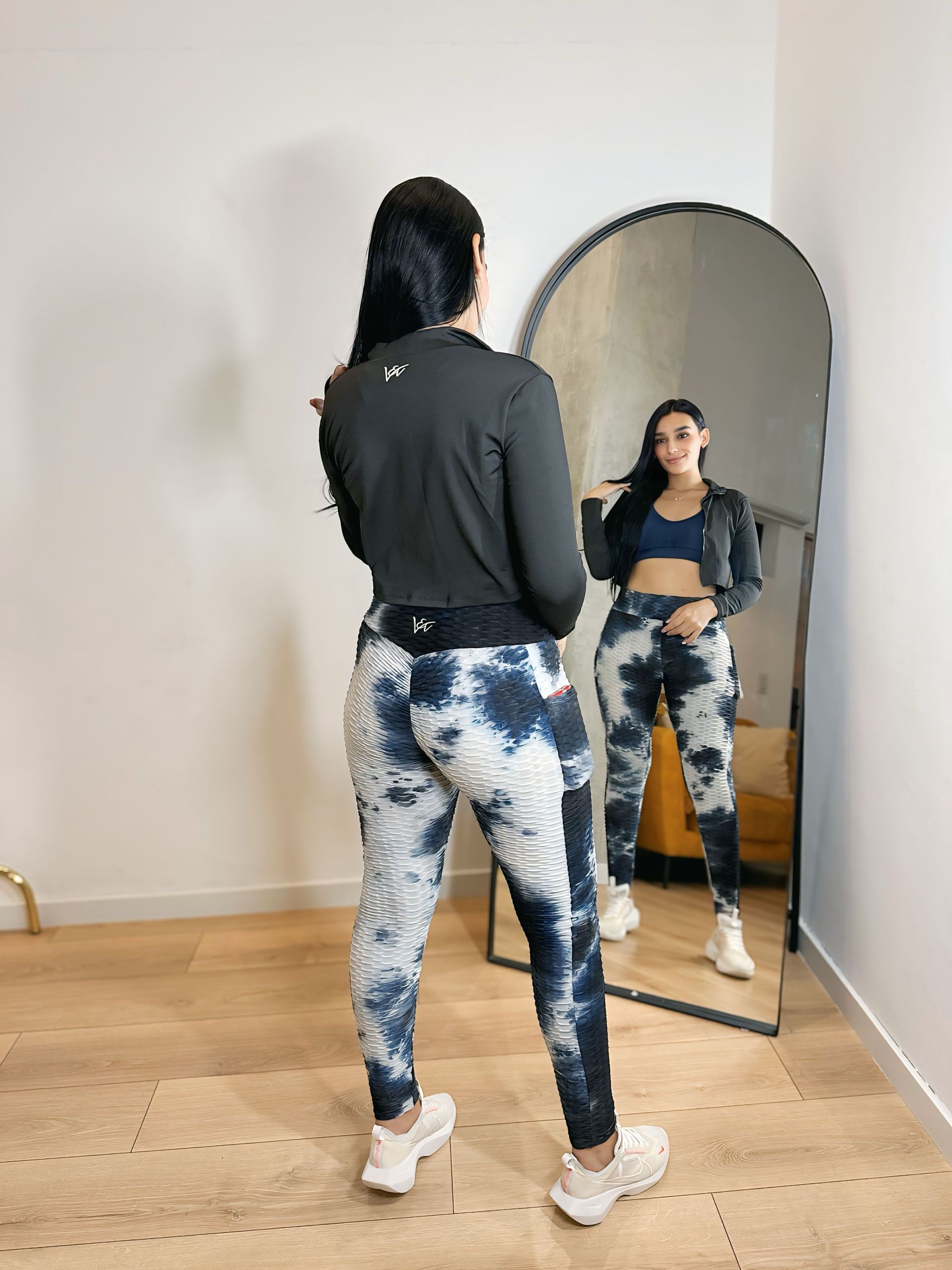 A woman is standing in front of a mirror wearing tie dye pants.