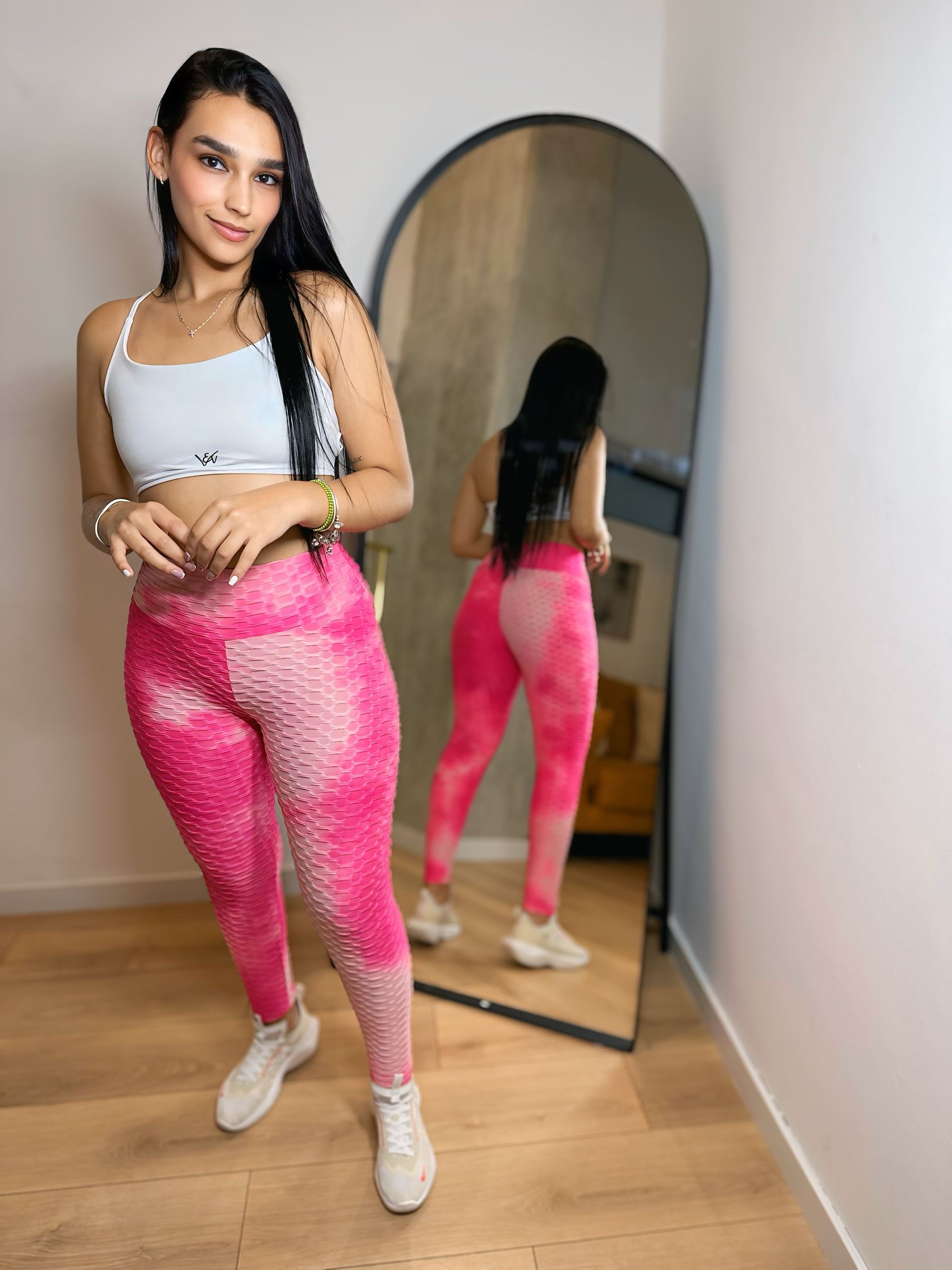 A woman is standing in front of a mirror wearing pink leggings.