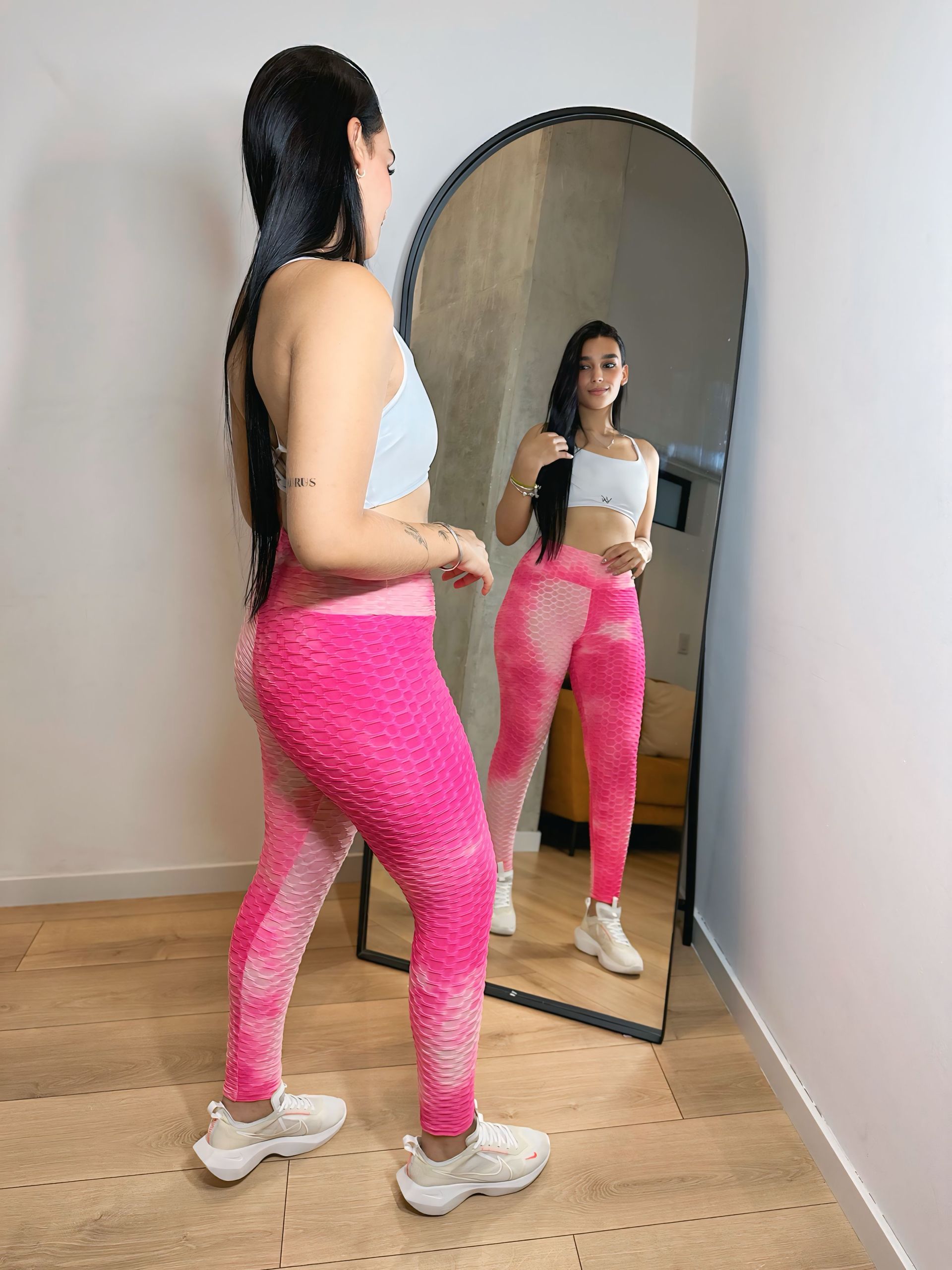 A woman in pink leggings is standing in front of a mirror.