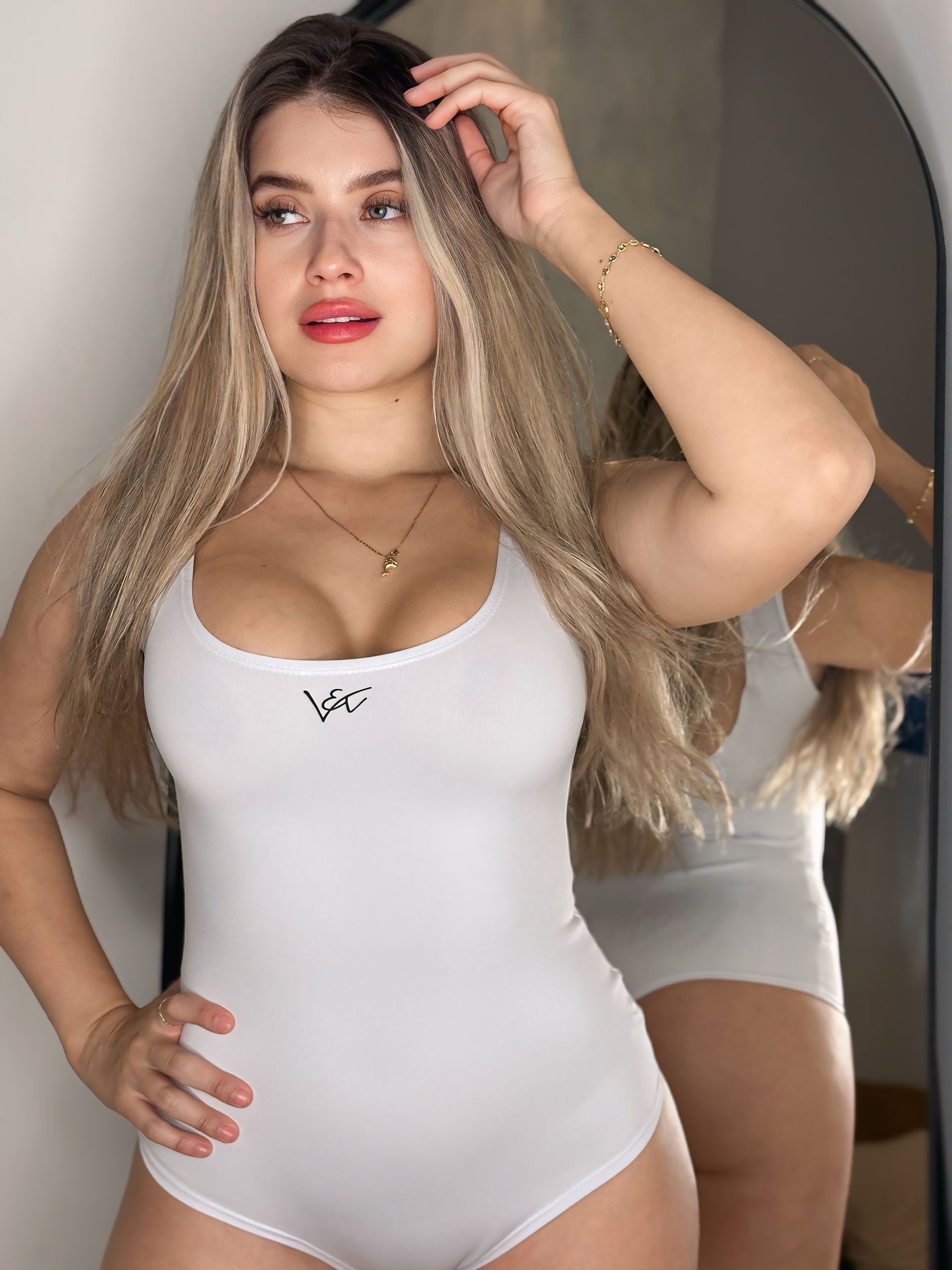 A woman in a white bodysuit is standing in front of a mirror.