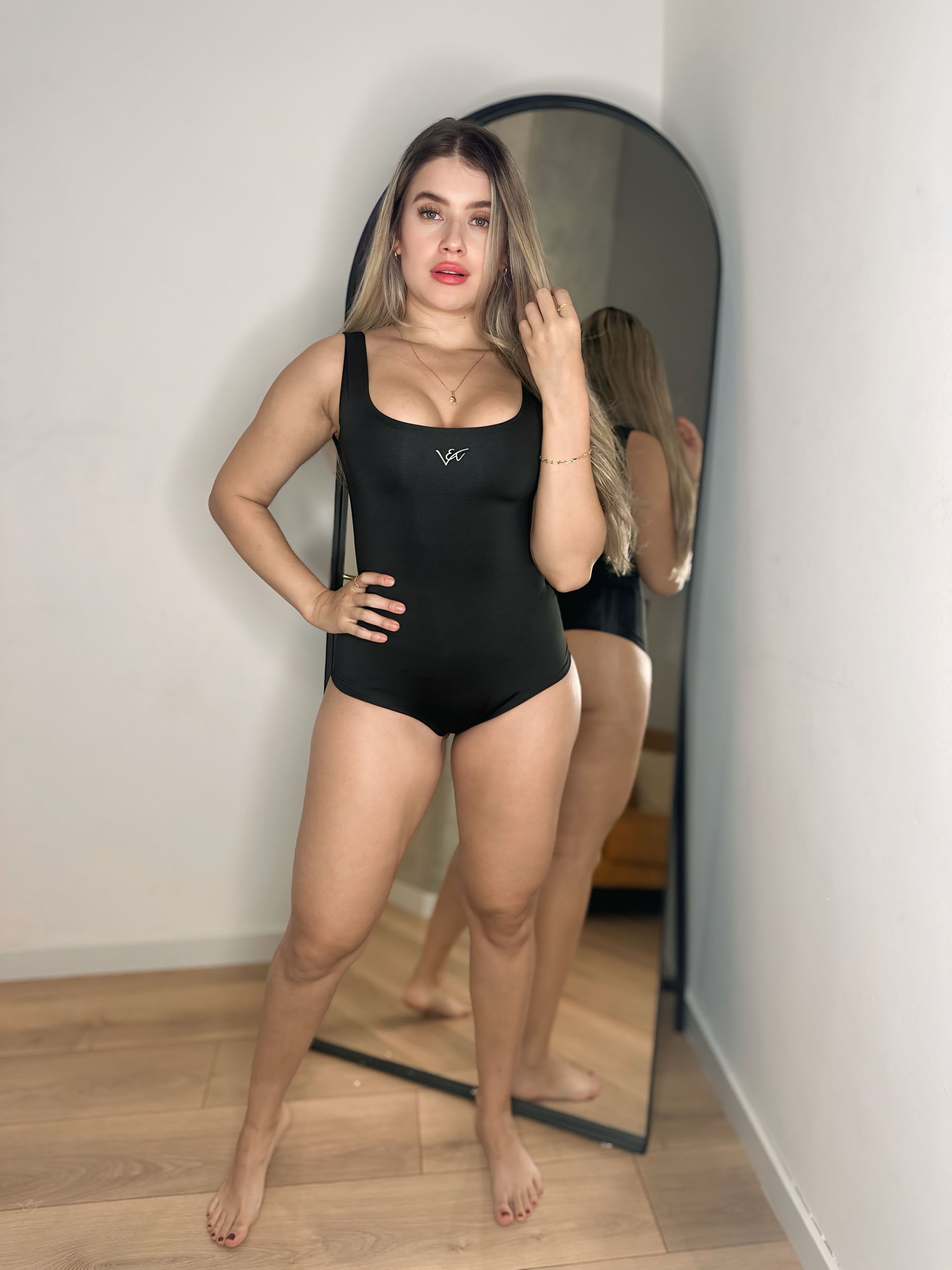 A woman in a black bodysuit is standing in front of a mirror.