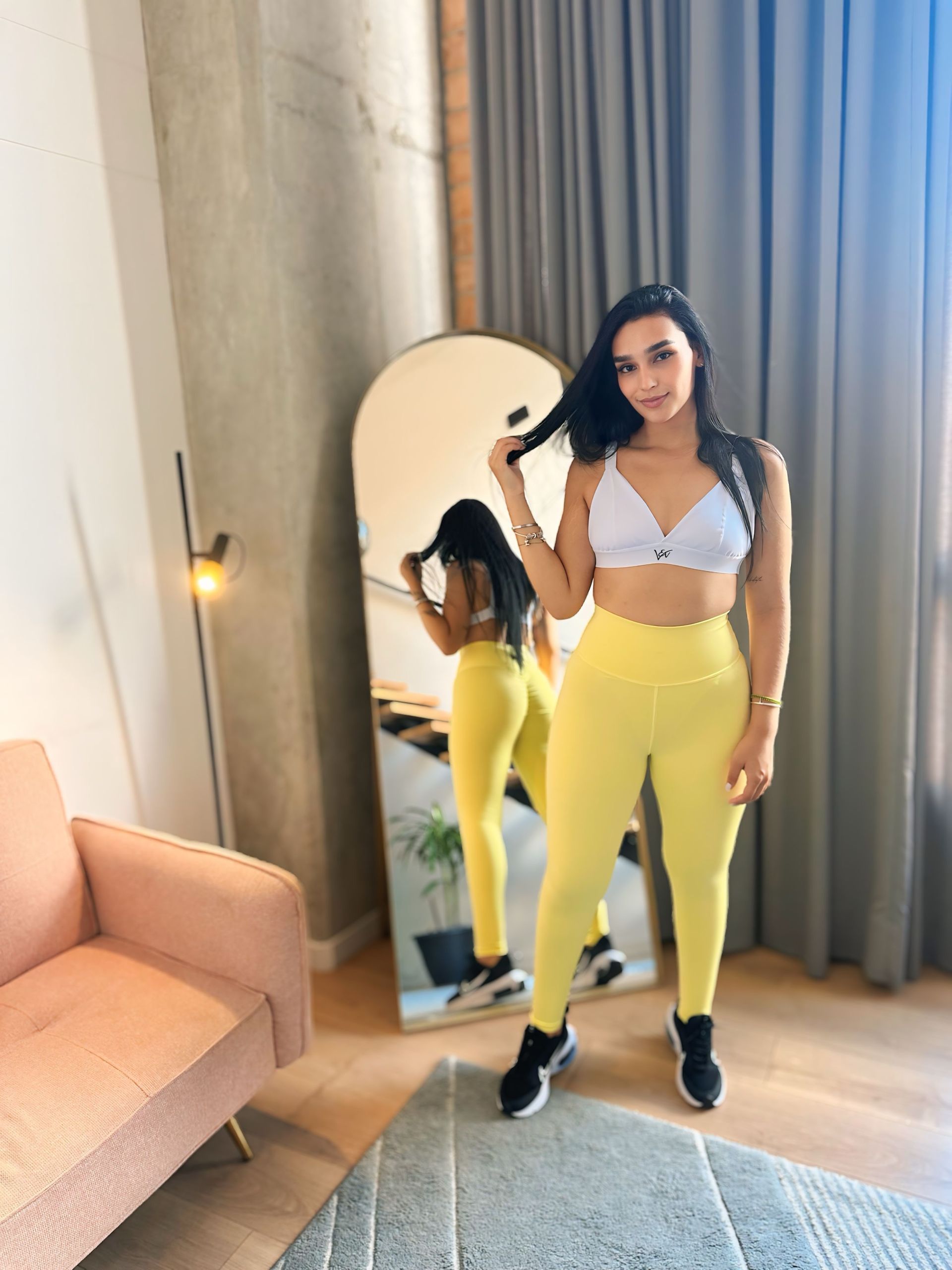 A woman is standing in front of a large mirror in a living room.