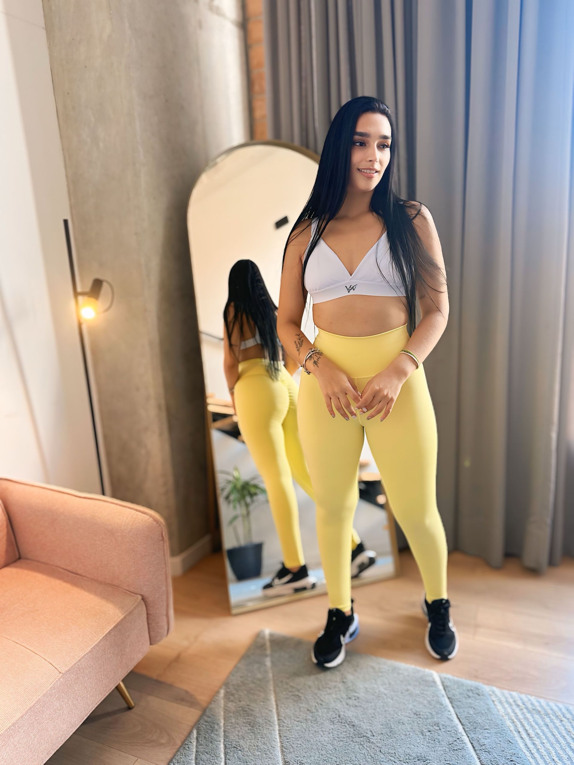 A woman is standing in front of a large mirror in a living room.