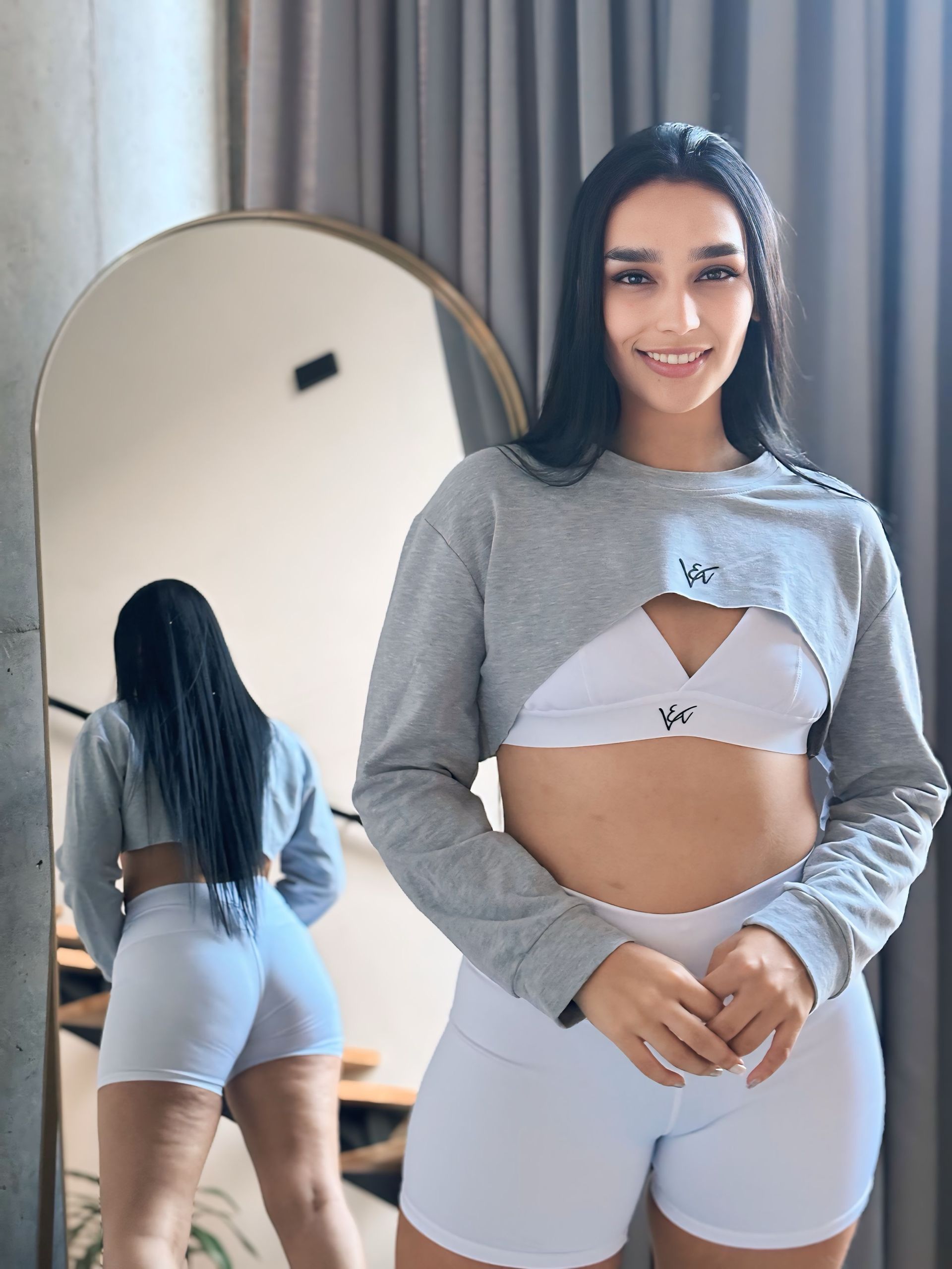 A woman in a crop top and white shorts is standing in front of a mirror.