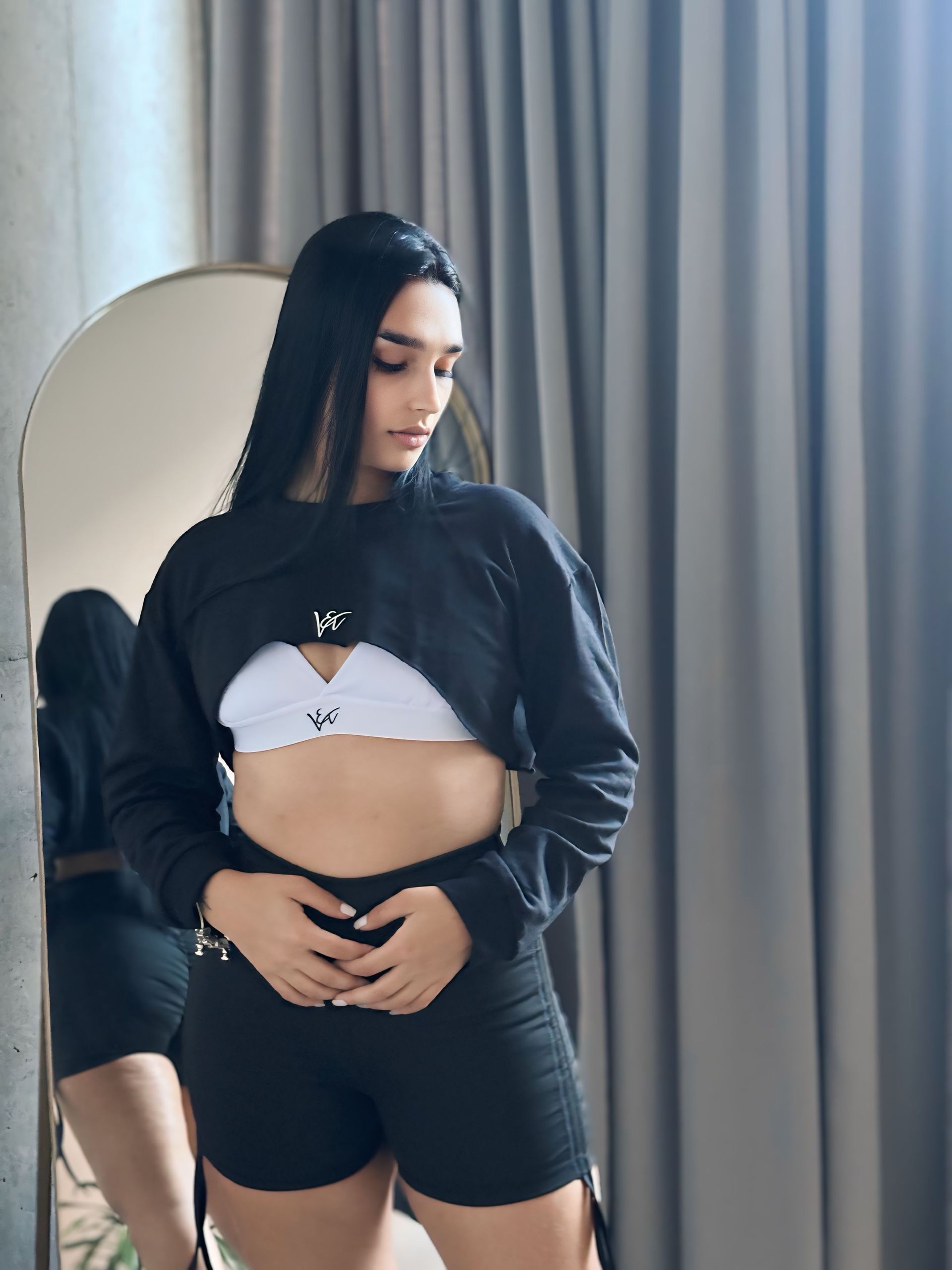 A woman in a crop top and shorts is standing in front of a mirror.