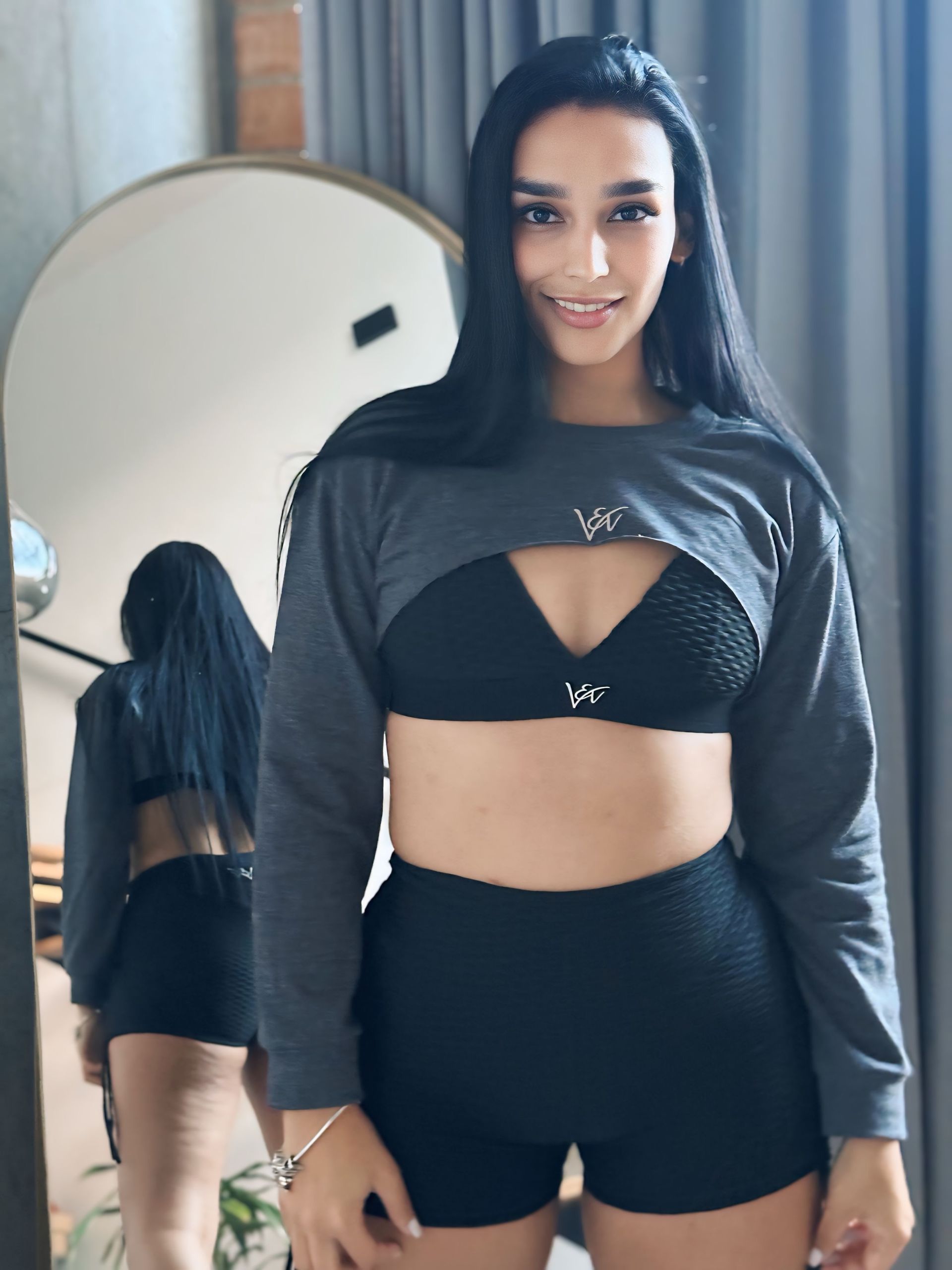 A woman in a crop top and shorts is standing in front of a mirror