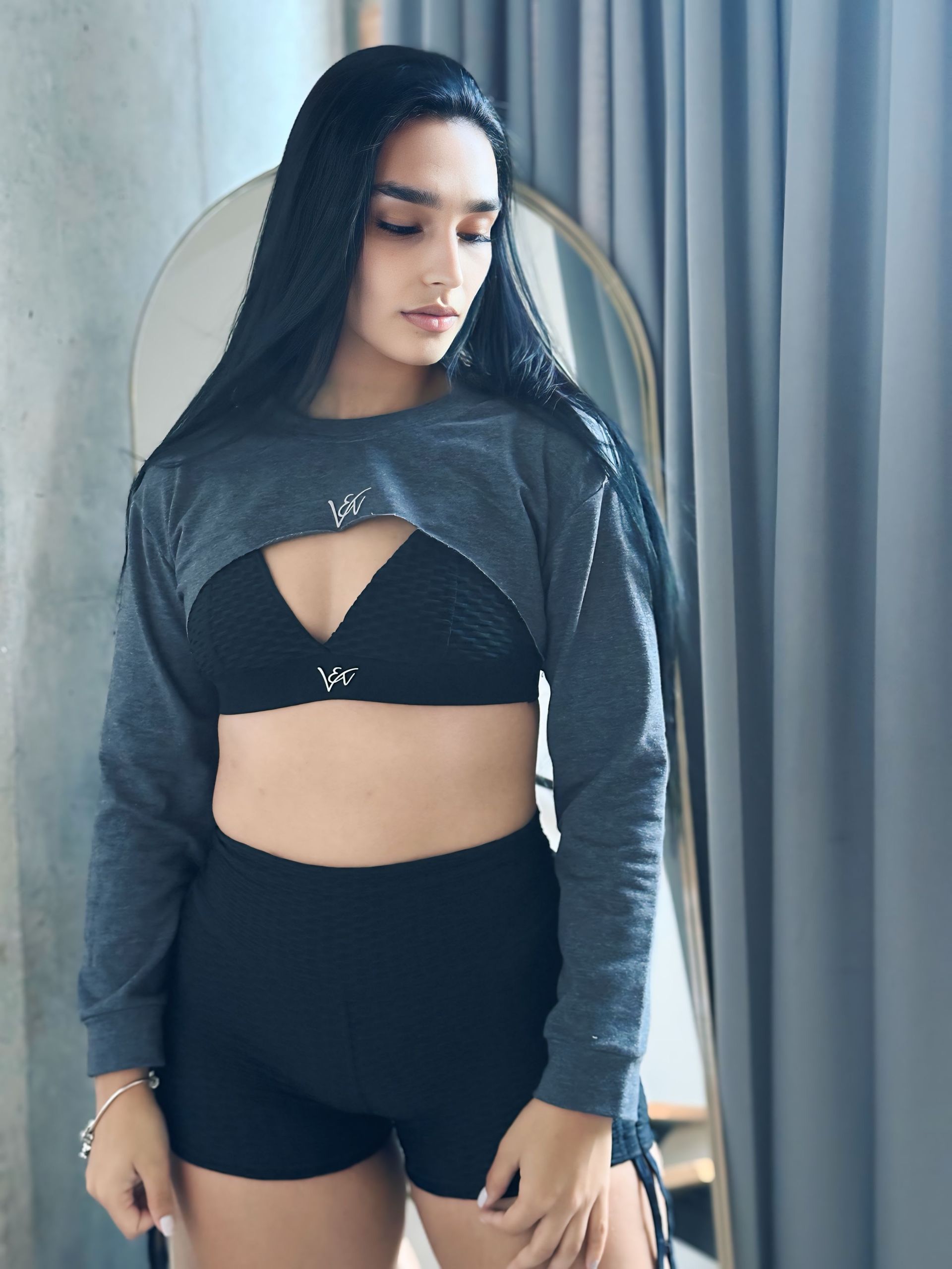 A woman in a crop top and shorts is standing in front of a mirror.