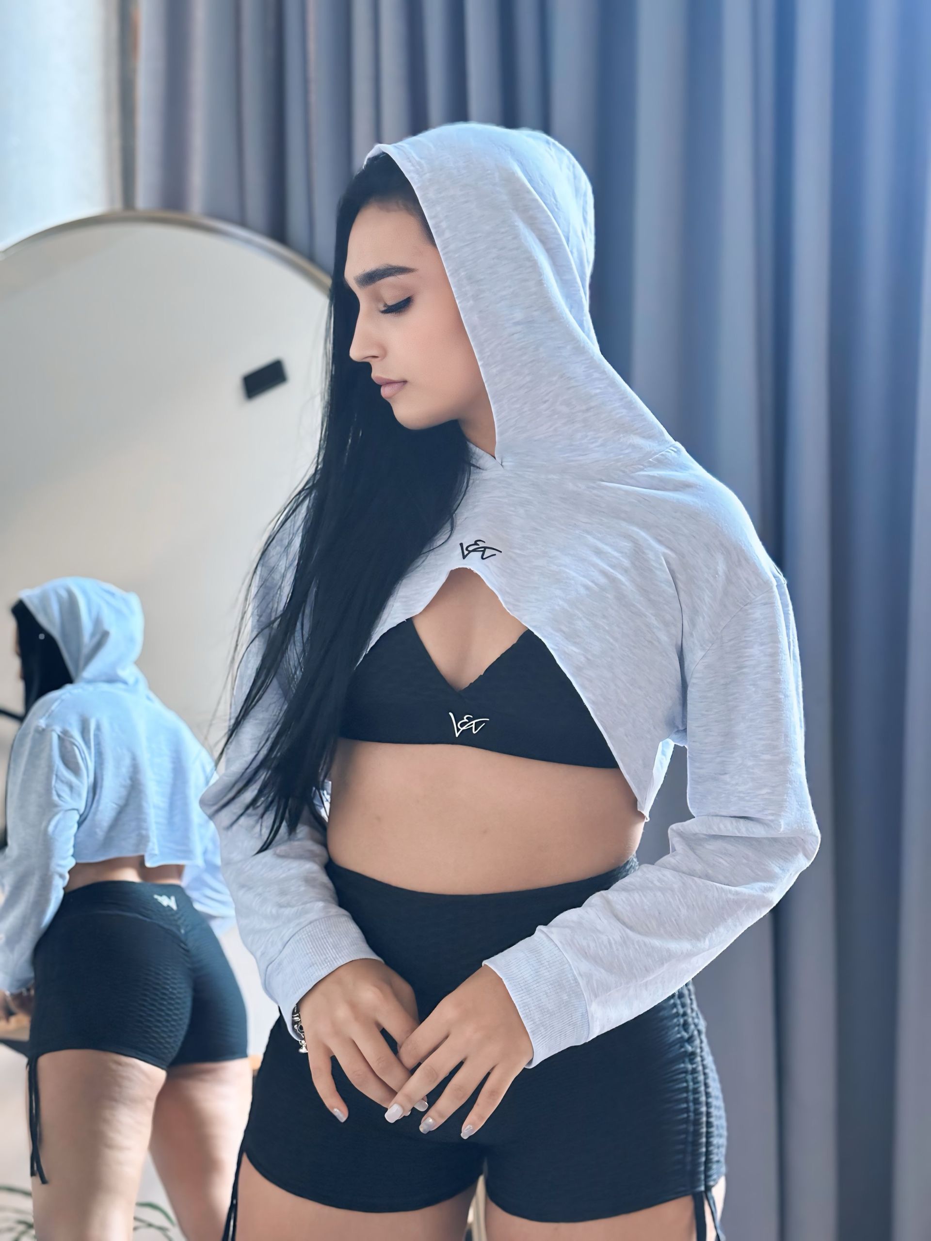 A woman in a crop top and shorts is standing in front of a mirror.