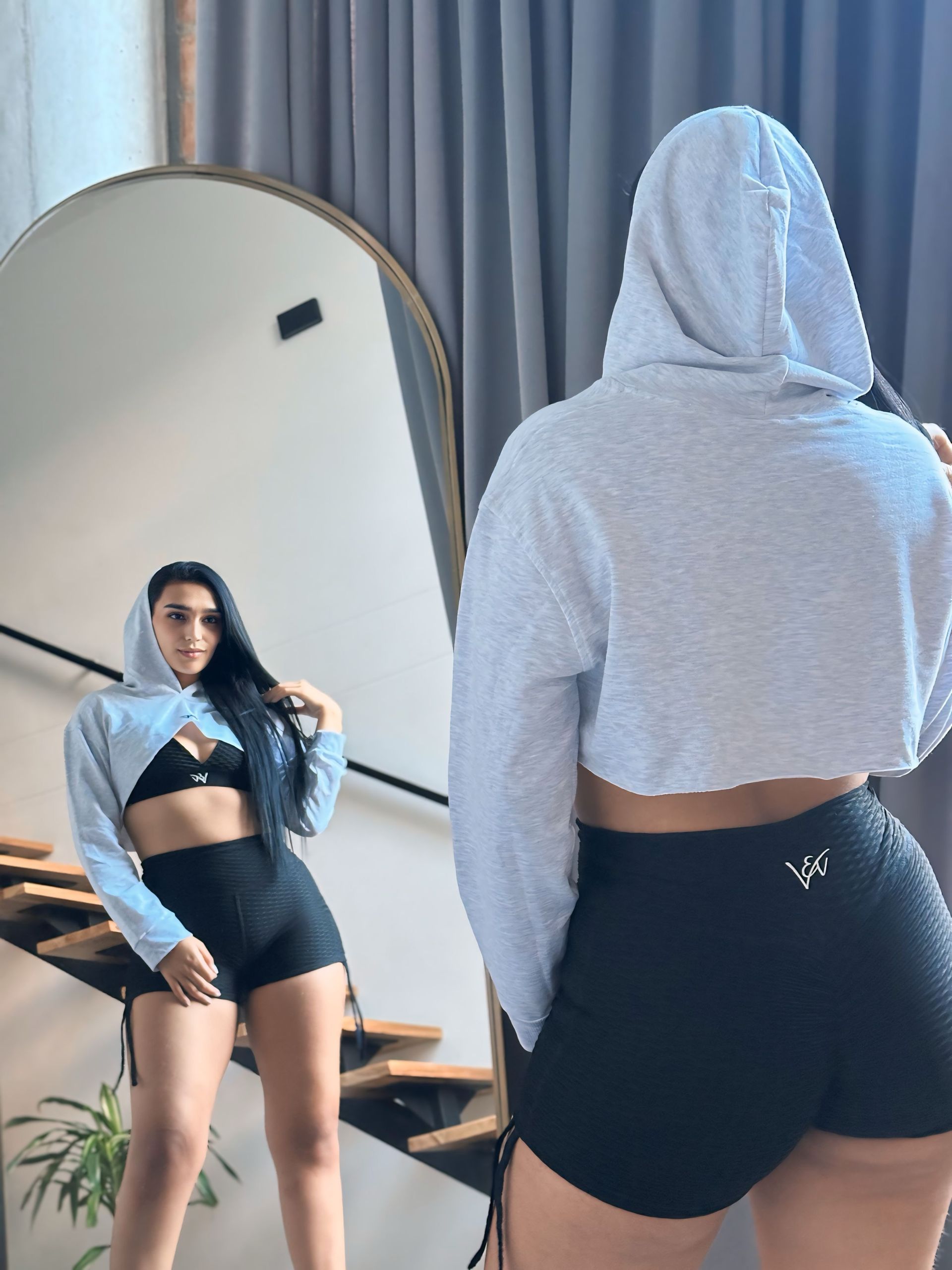 A woman in a crop top and shorts is standing in front of a mirror.