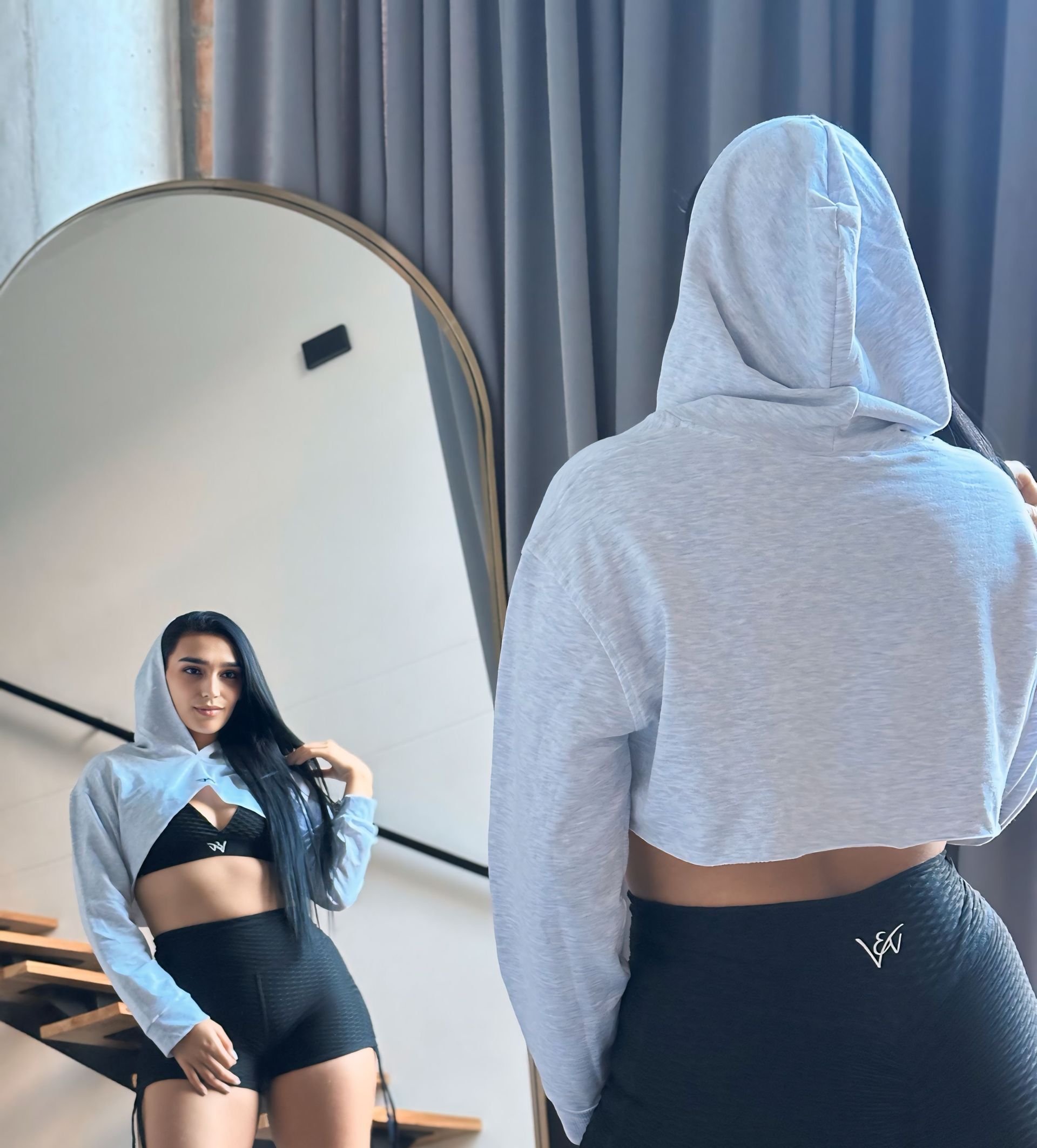 A woman in a crop top and shorts is standing in front of a mirror