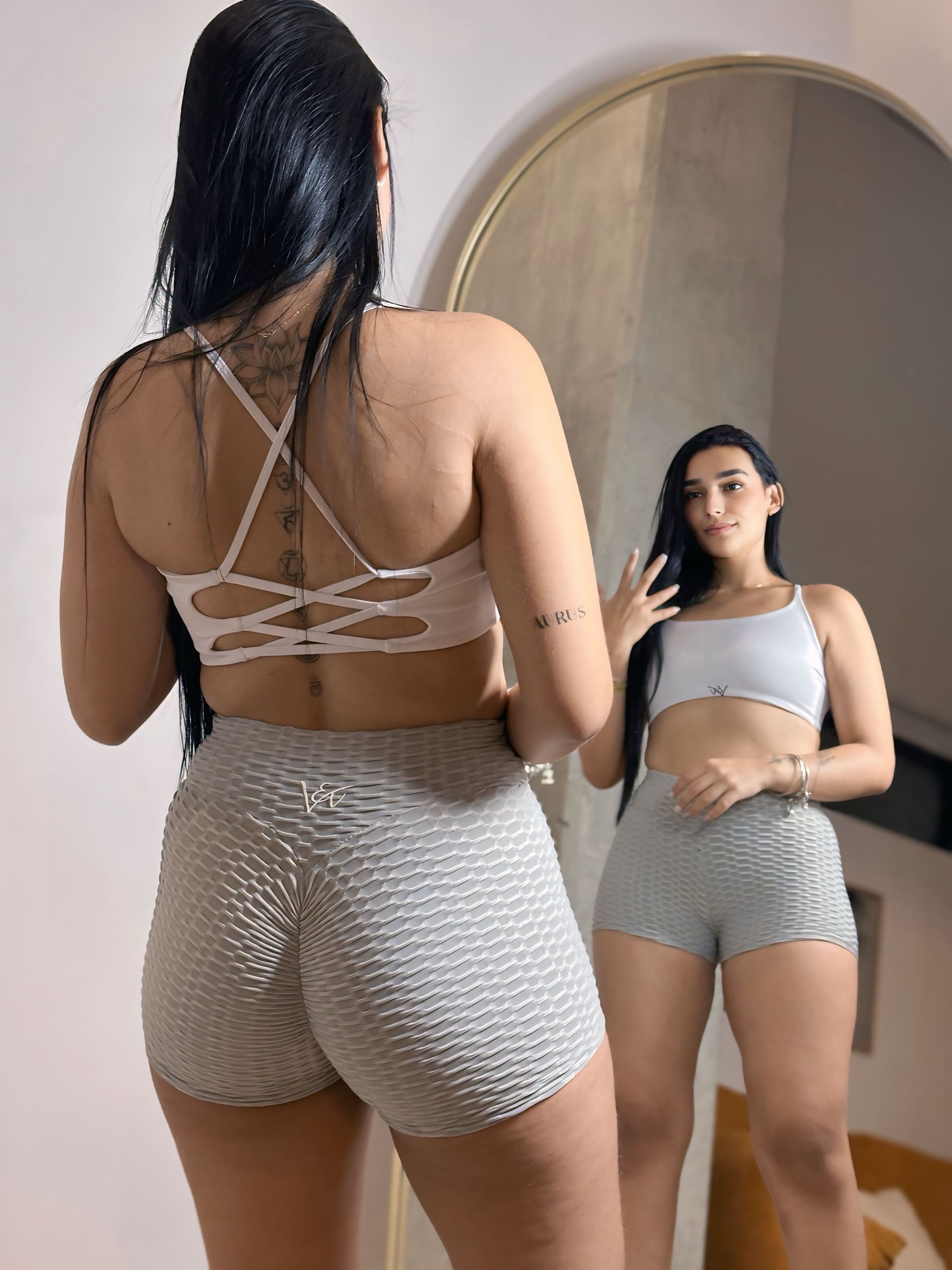 A woman is standing in front of a mirror wearing shorts and a crop top.