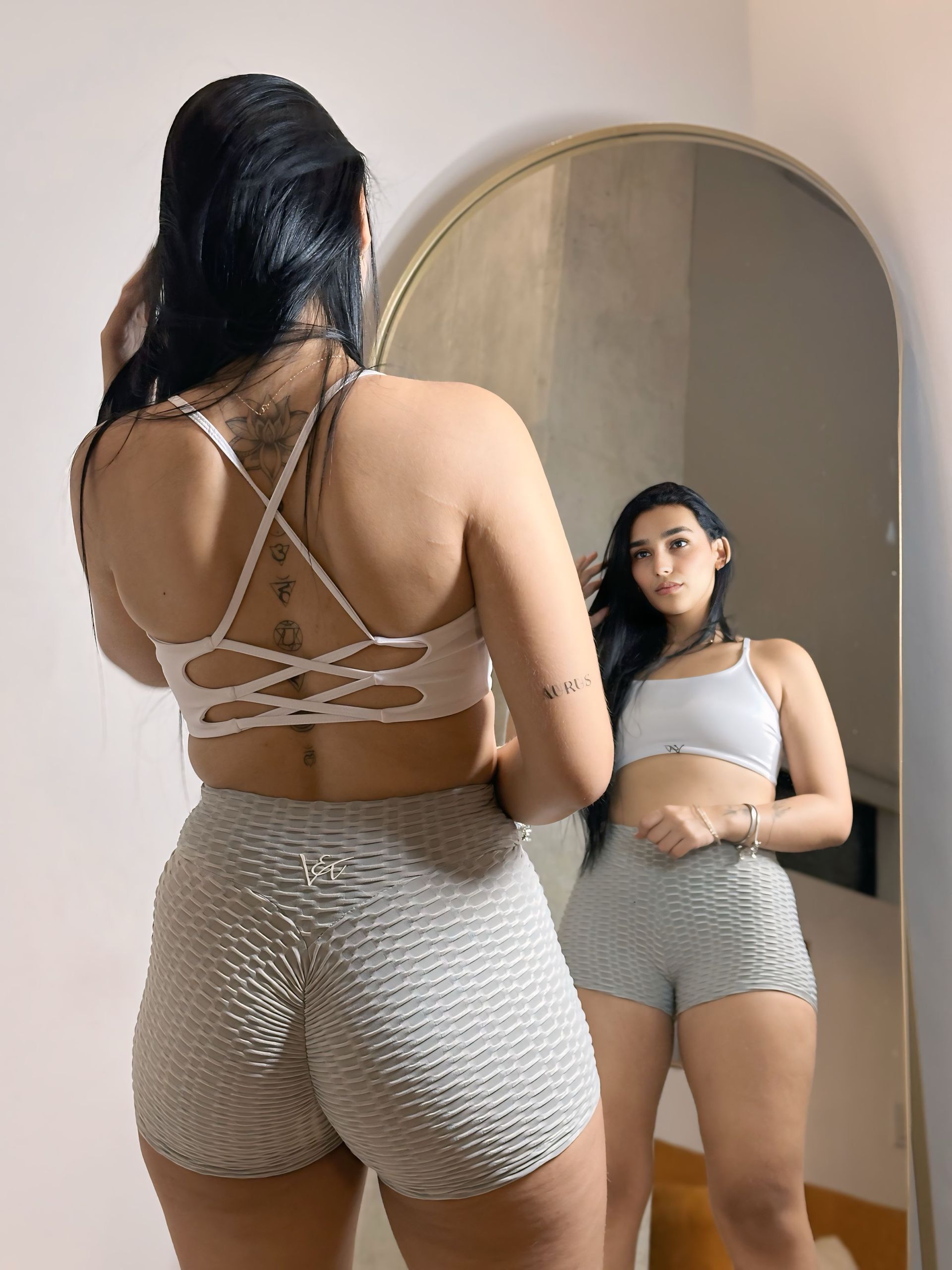 A woman is standing in front of a mirror wearing shorts and a crop top.