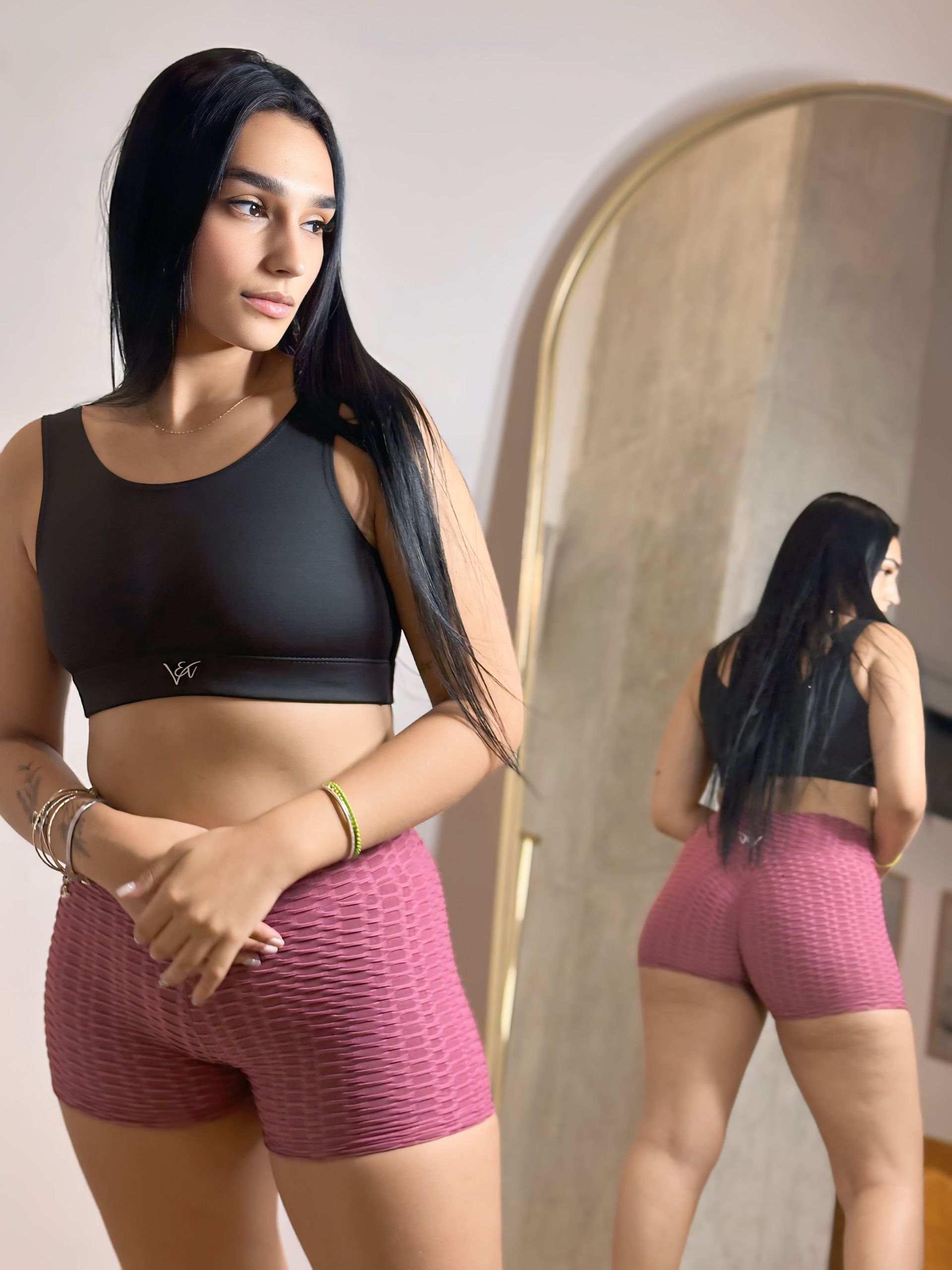 A woman in a black top and pink shorts is standing in front of a mirror.