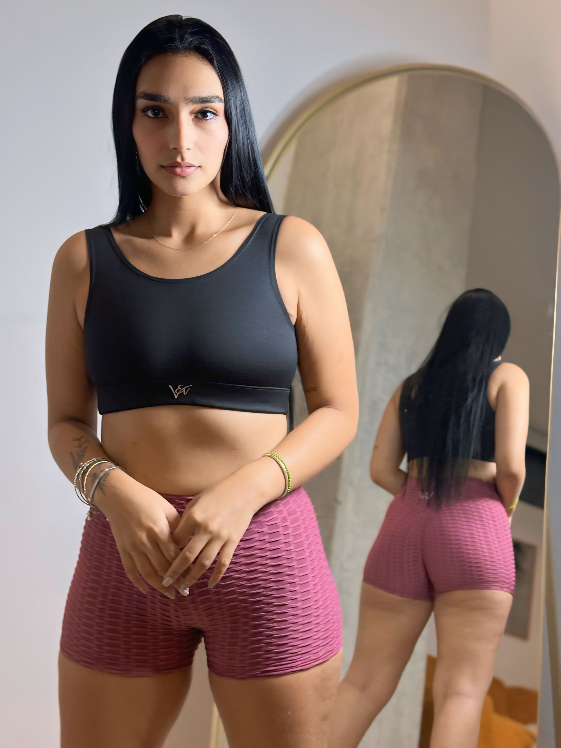 A woman in a black top and pink shorts is standing in front of a mirror.